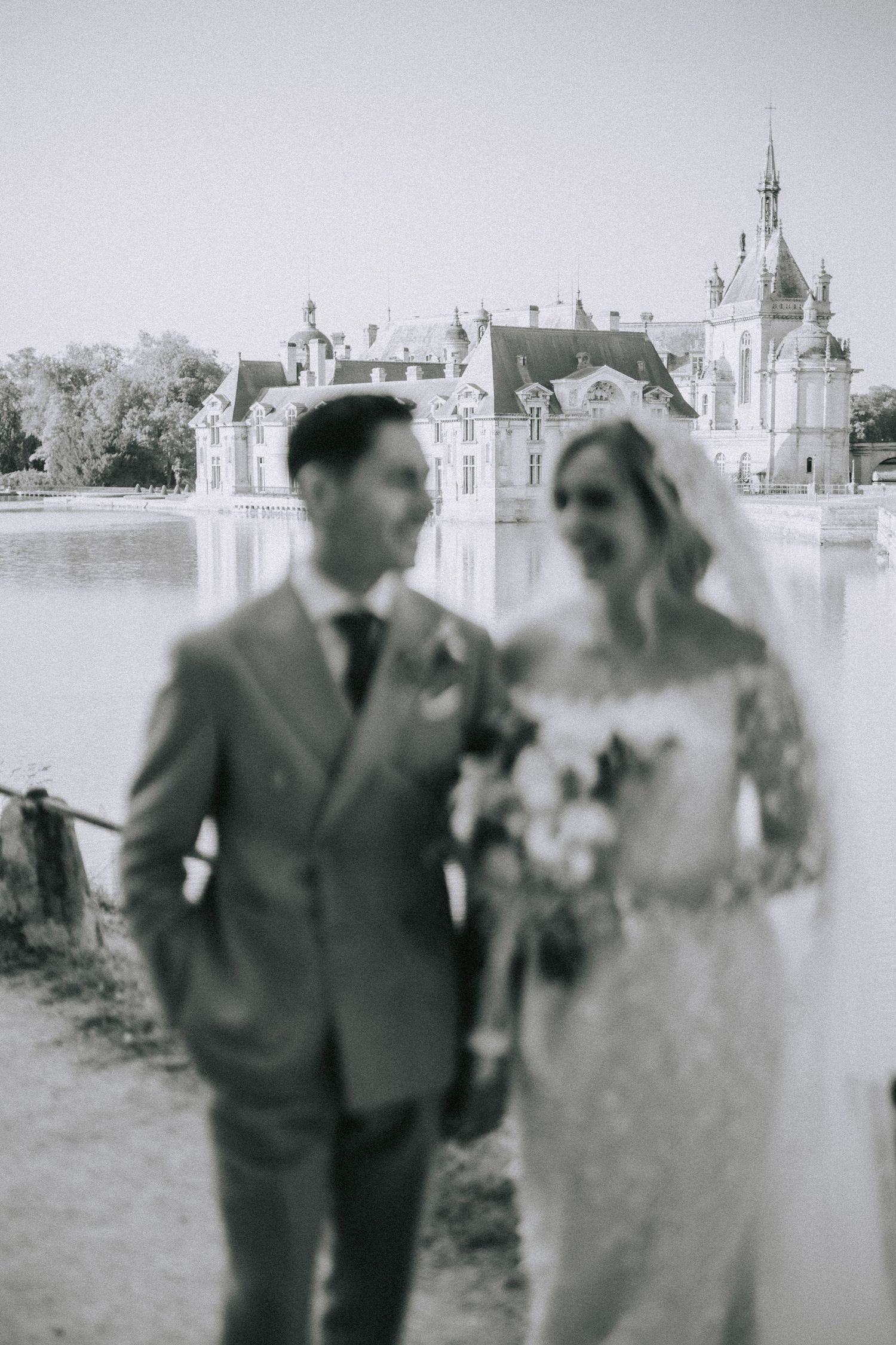 A vintage black and white wedding photo taken in front of an ornate palace or chateau with spires and decorative architecture.