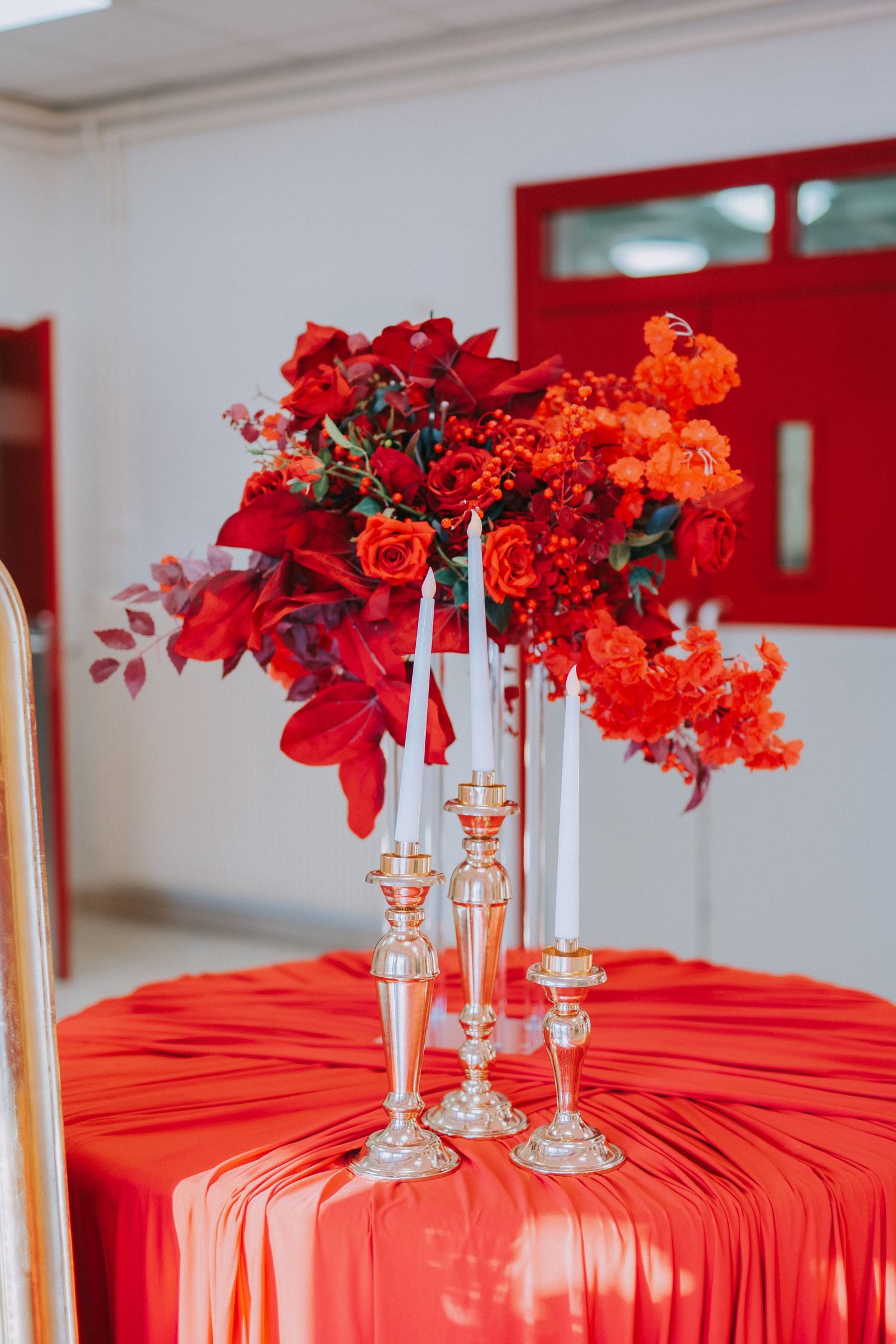 Elegant red and orange floral centerpiece on red tablecloth with crystal candle holders.