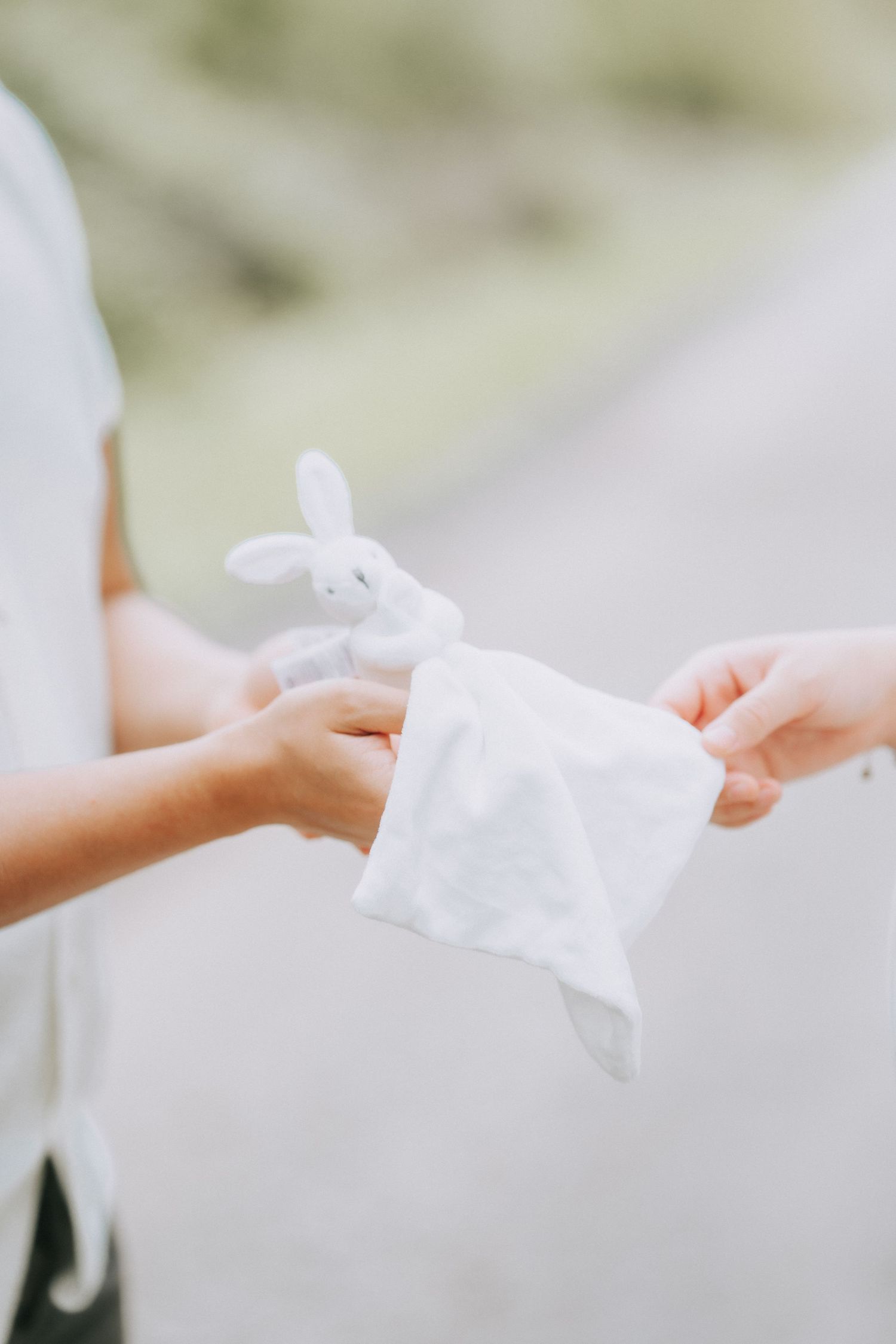 Hands exchanging a small white bundle with a decorative bunny detail.