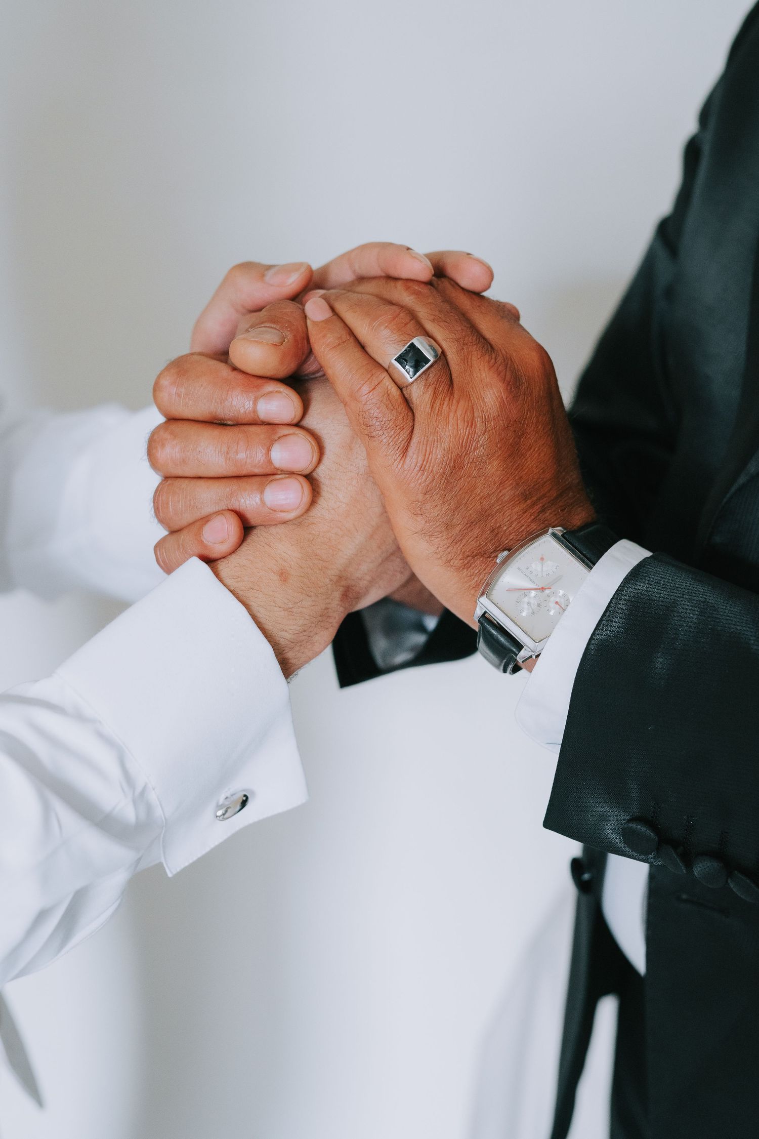 A close-up of clasped hands showing a ring and watch detail during a formal occasion.