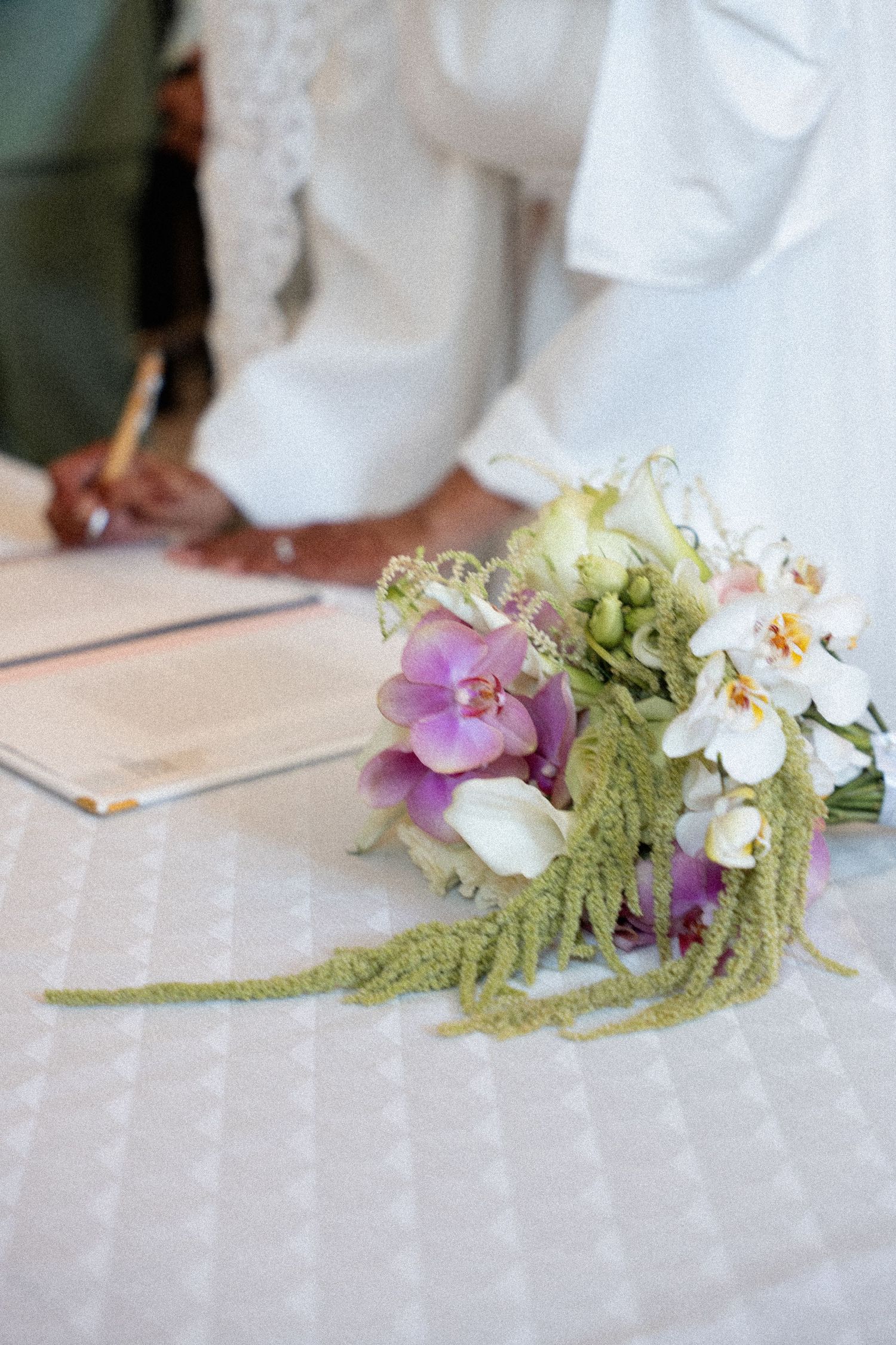 A delicate floral arrangement with white orchids and green ferns lies on a light-colored surface.