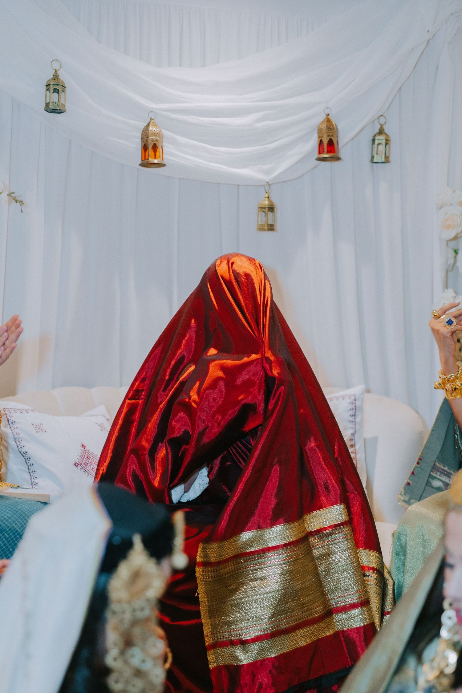 Red and gold traditional garment with hanging lantern decorations against white drapes.
