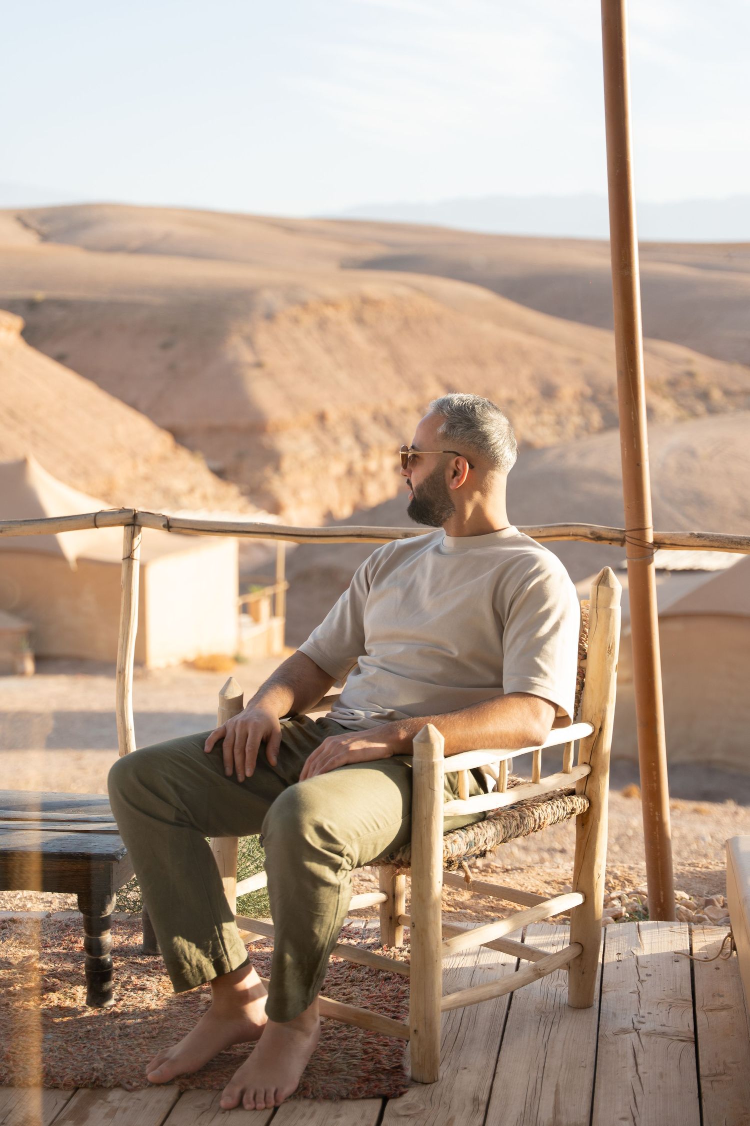 Person relaxing on wooden chair overlooking desert mountains during sunset.