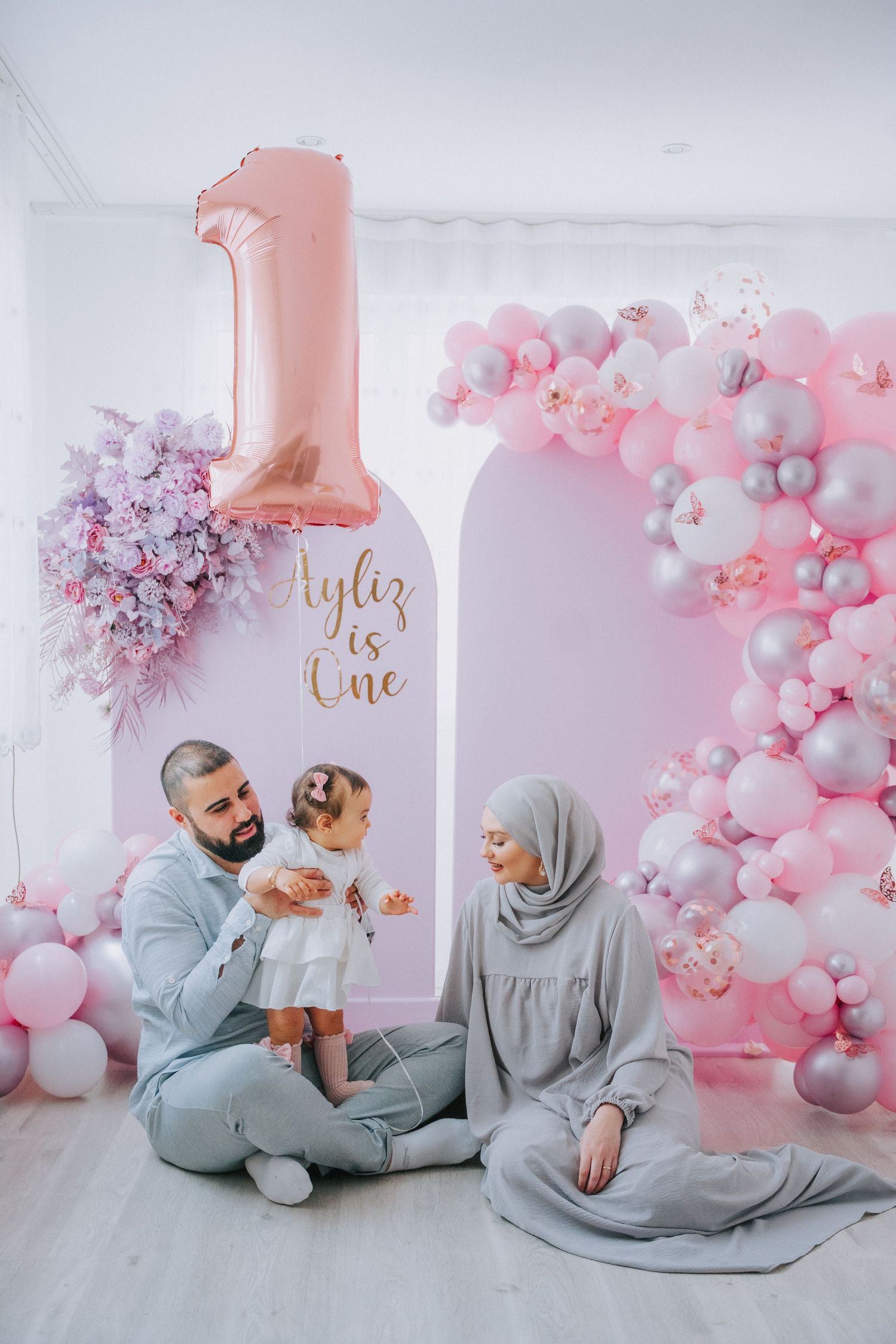Family photoshoot with pink balloon arch and rose gold number one balloon backdrop.