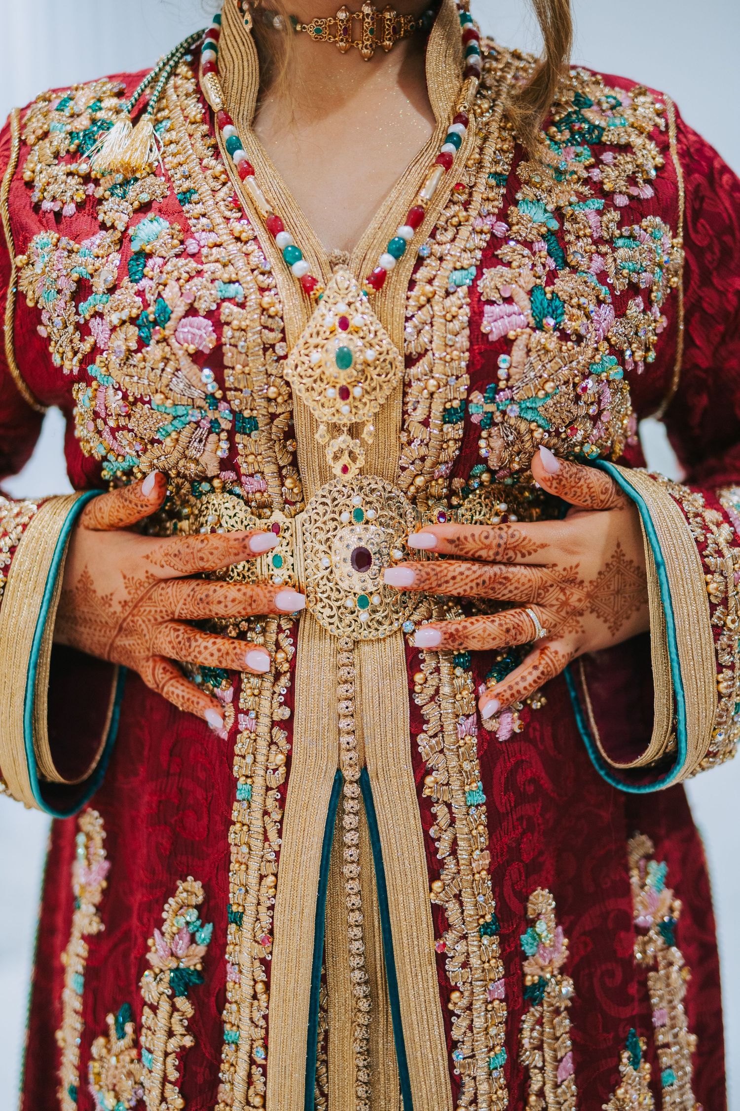Ornate red traditional dress with intricate gold embroidery and turquoise details, decorated hands painted with henna shown.