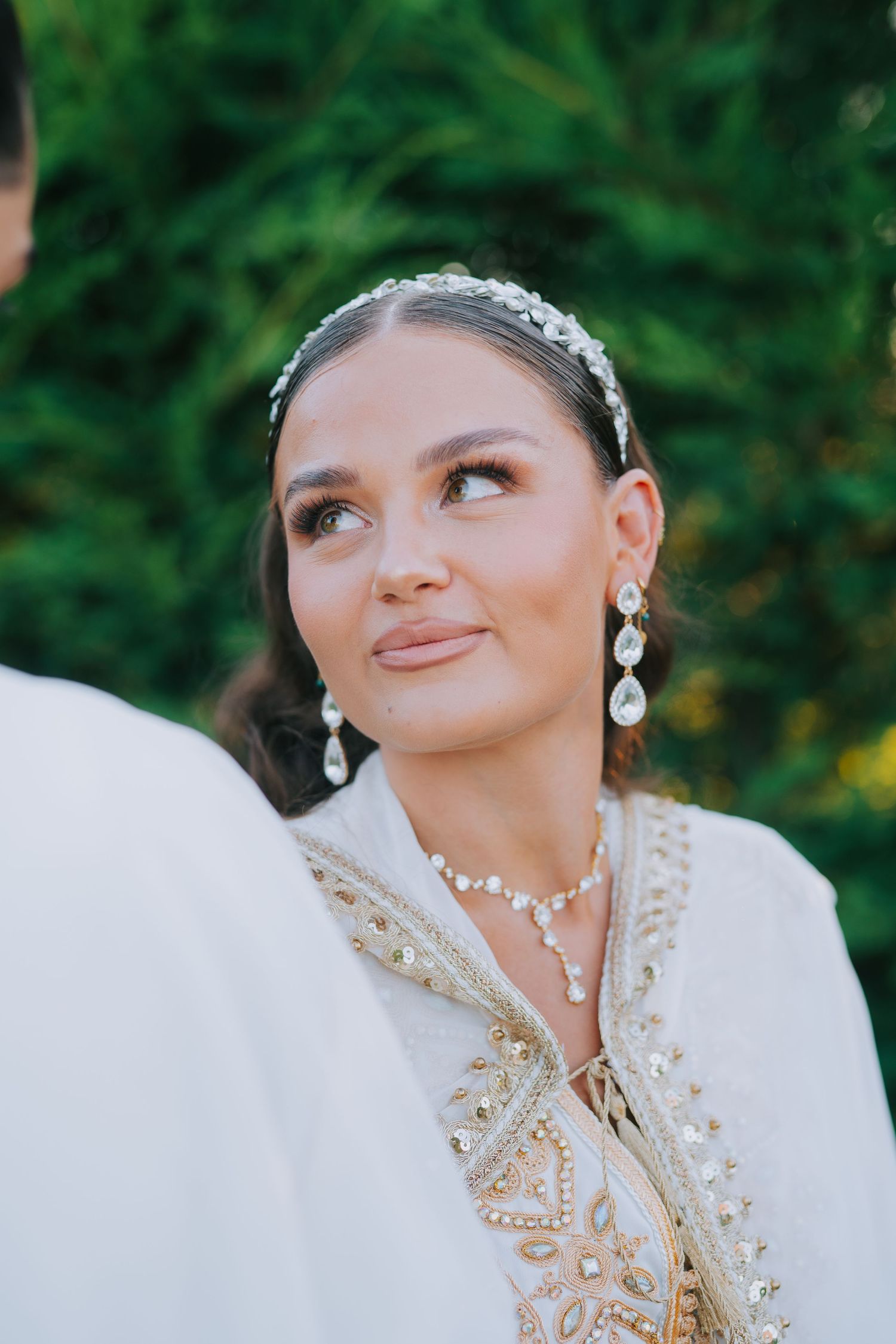 Close-up of bride wearing crystal headpiece and ornate white gown with gold embellishments.
