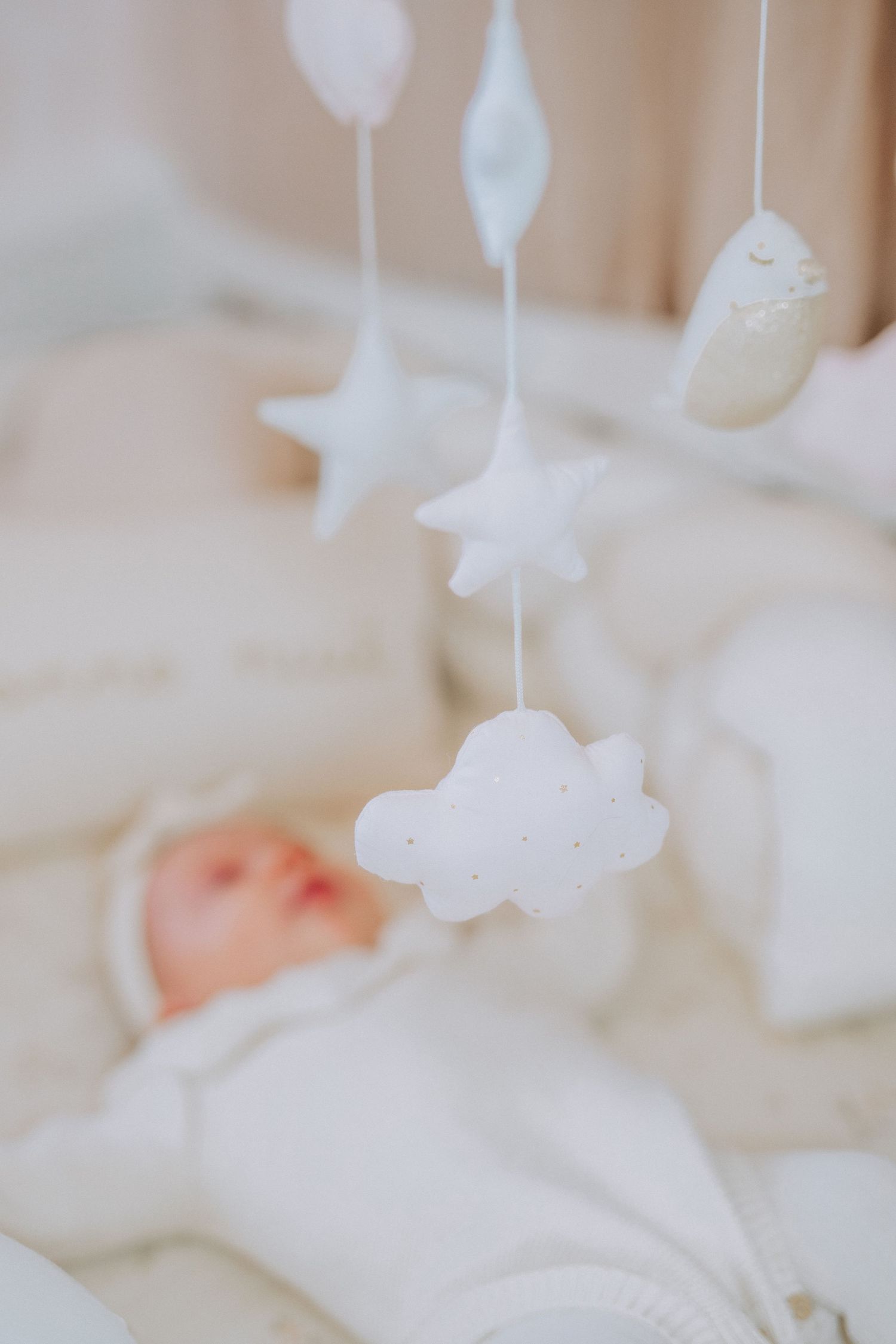 White hanging star and cloud mobile decorations over soft bedding.