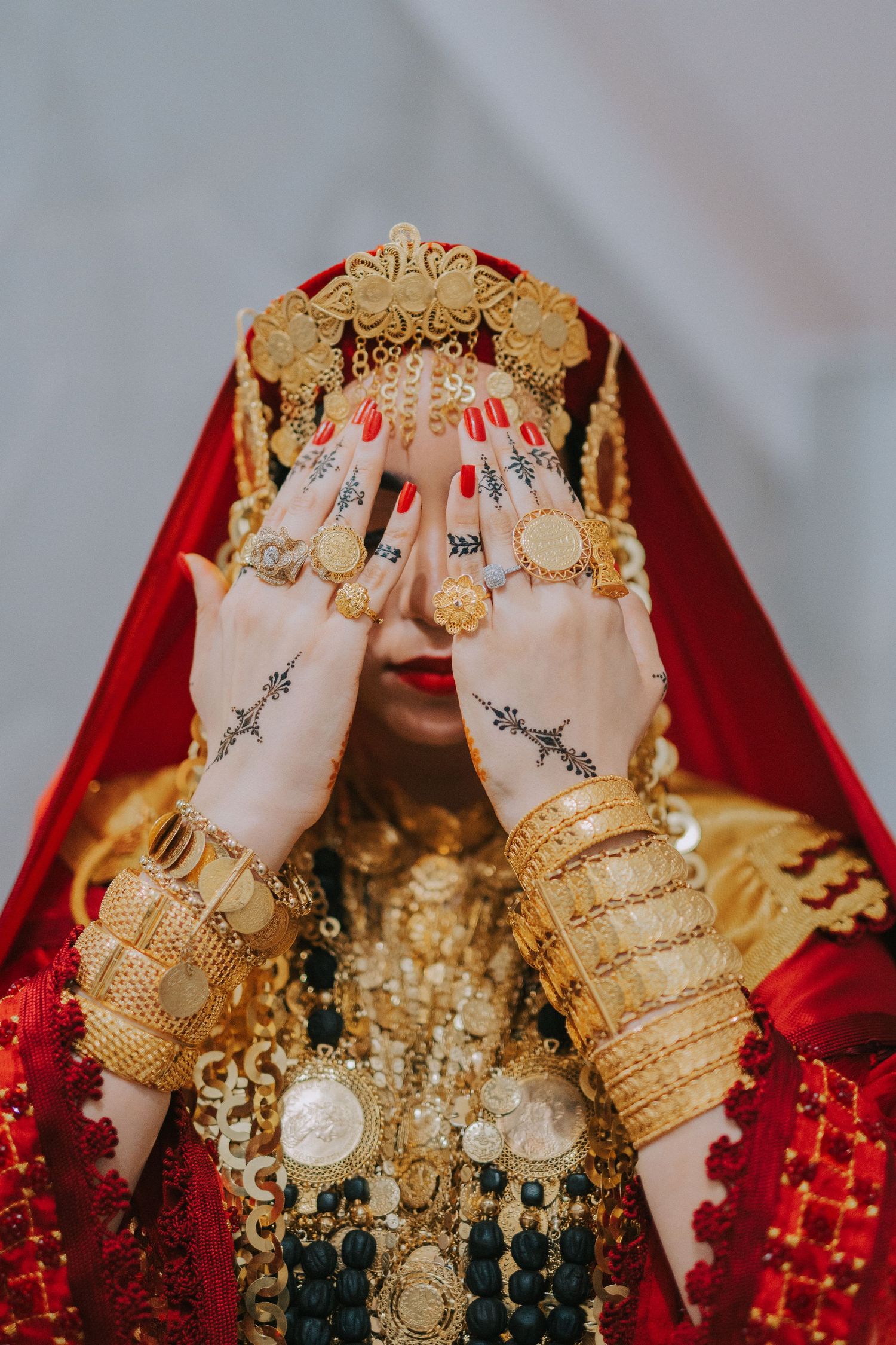 Traditional bride's hands adorned with gold bracelets and henna designs under a red veil.