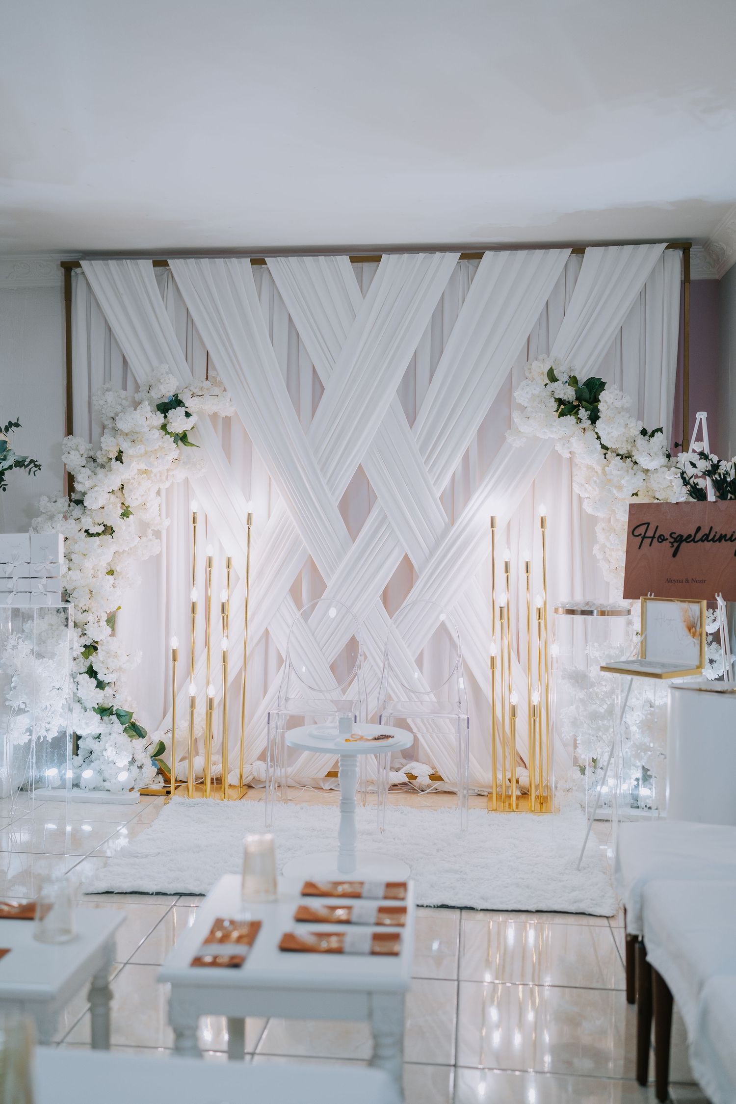 Elegant white wedding backdrop with crossed fabric panels and golden candle holders.