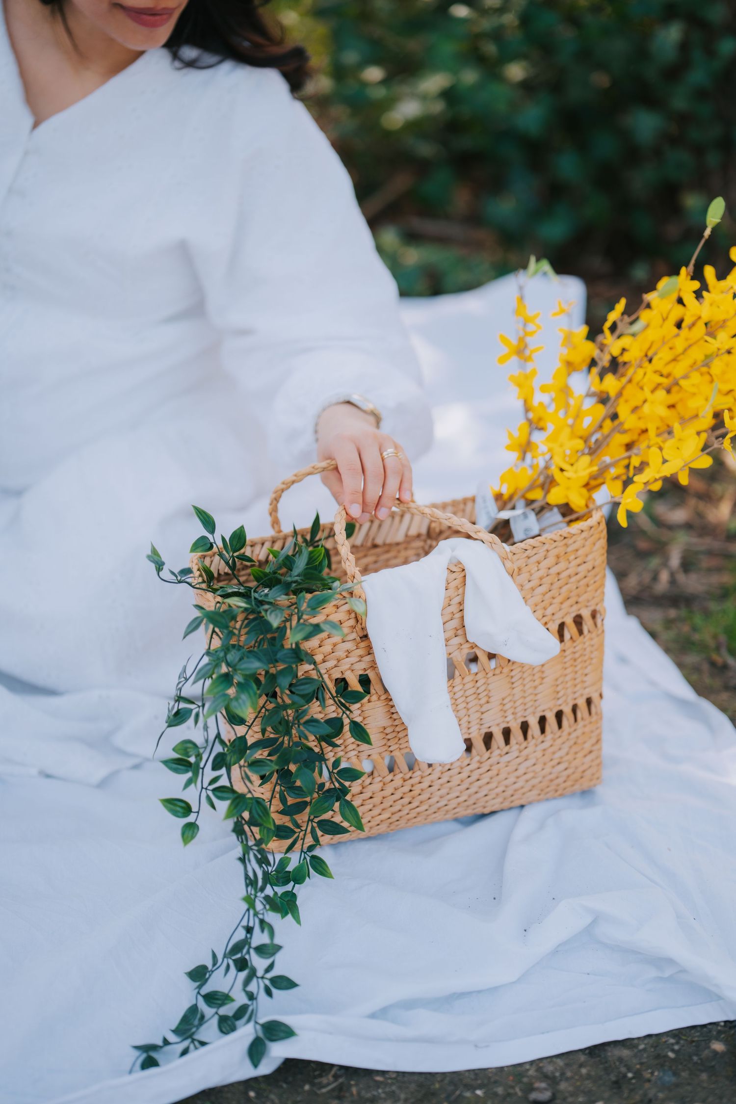 Wicker basket with baby items and yellow flowers against white dress background.