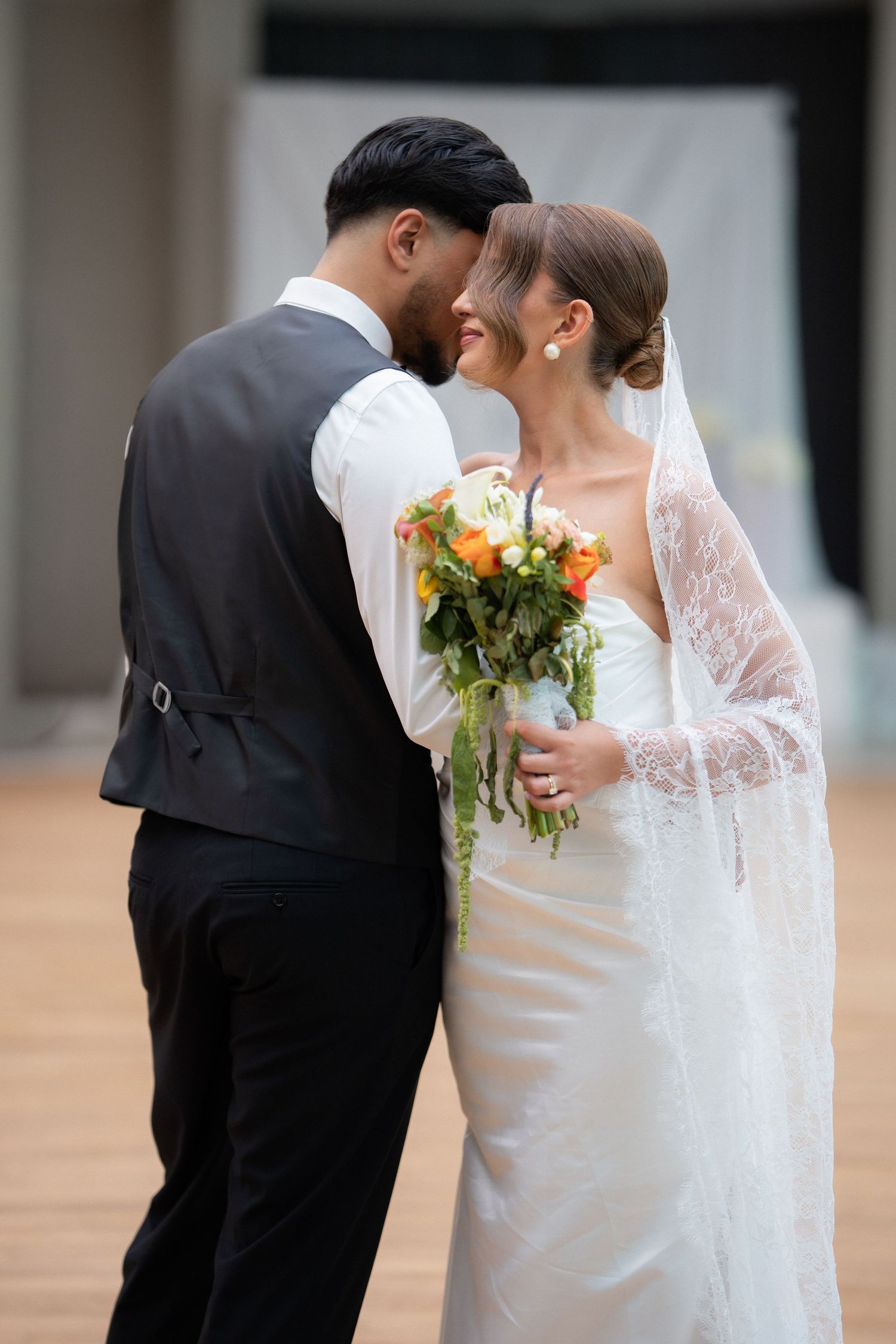 A romantic wedding couple shares an intimate kiss while holding a bouquet of flowers at an elegant venue.