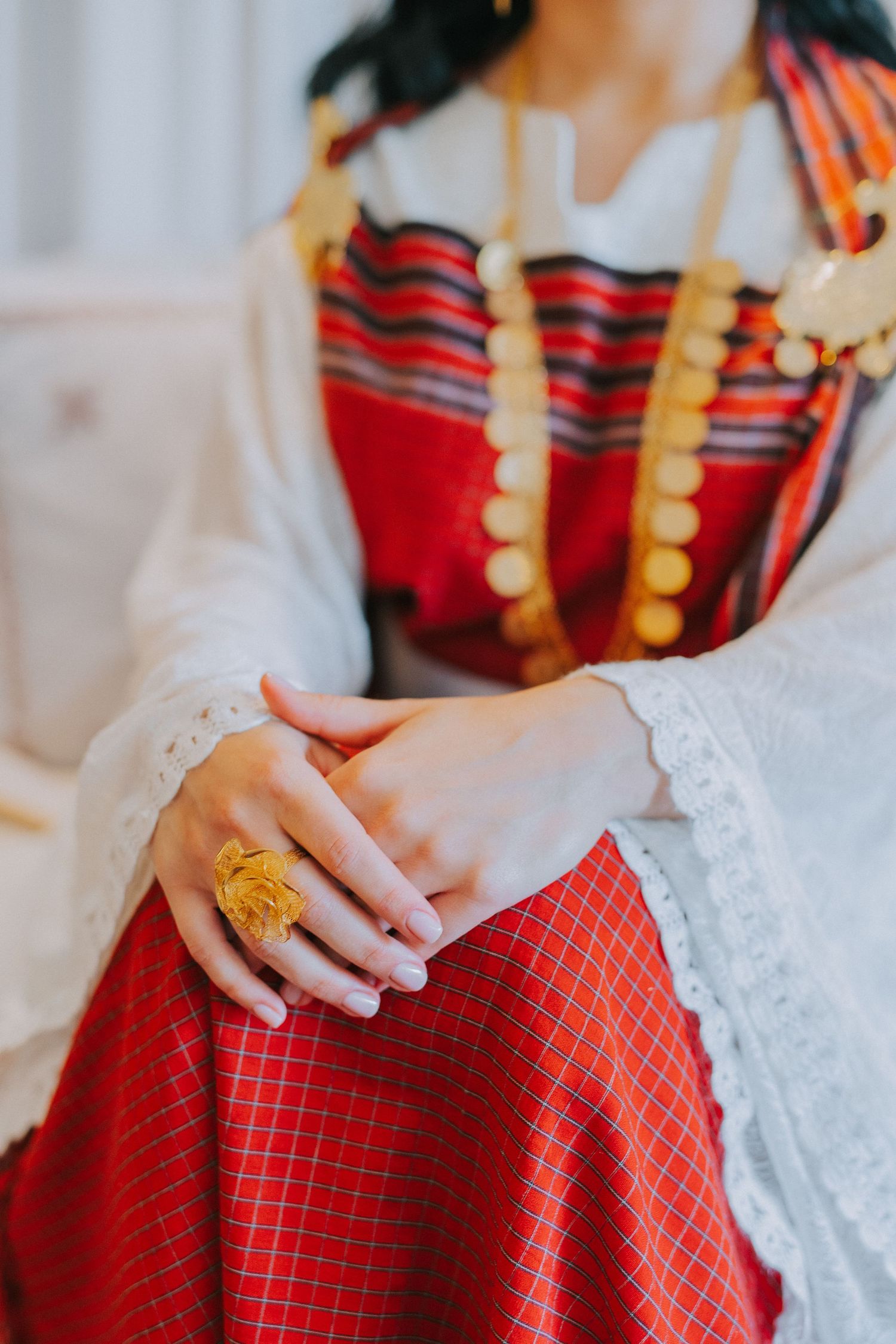 Traditional red and white dress with gold jewelry and lace details.