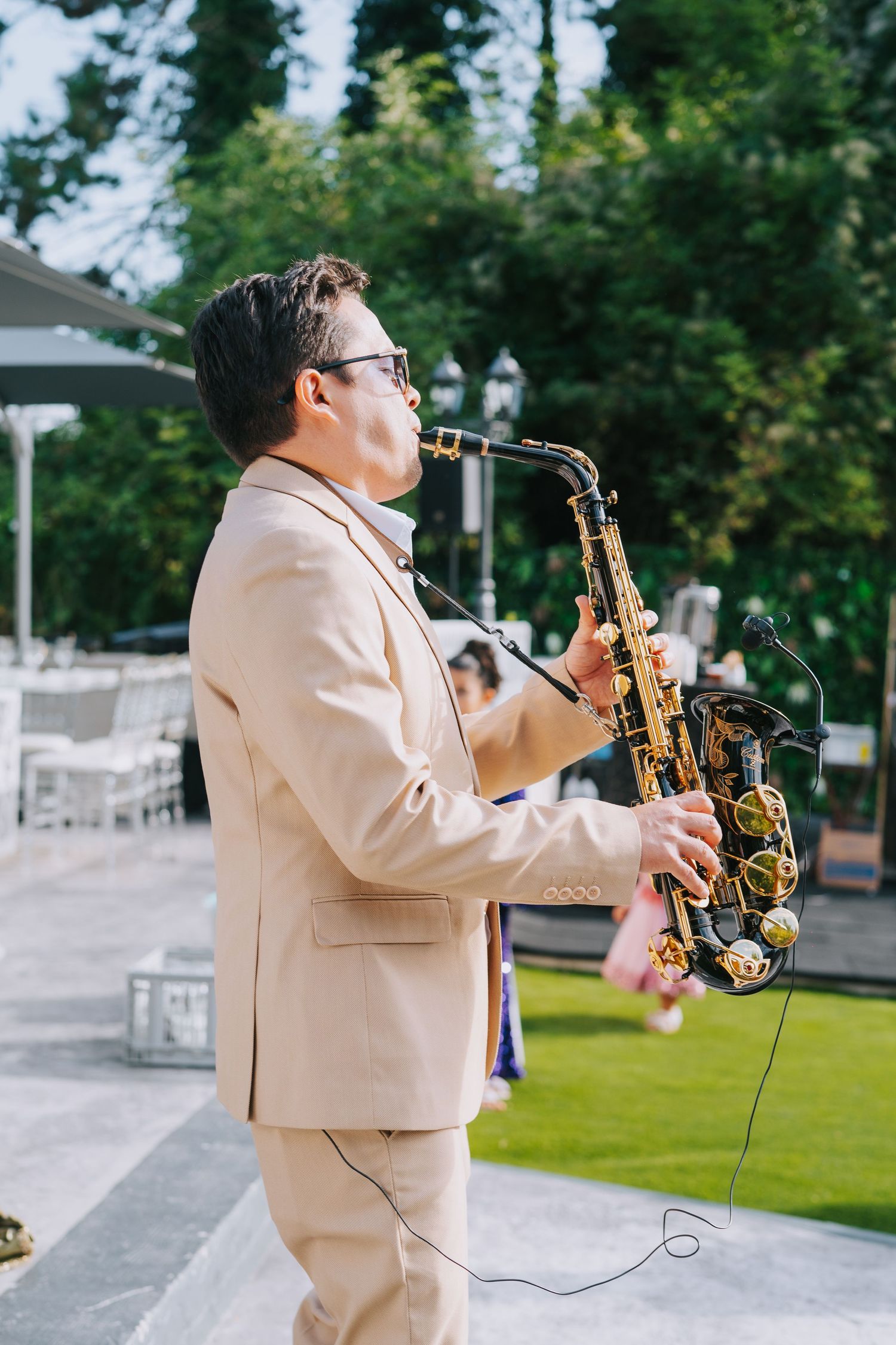 Musician in a beige suit playing saxophone during an outdoor performance.