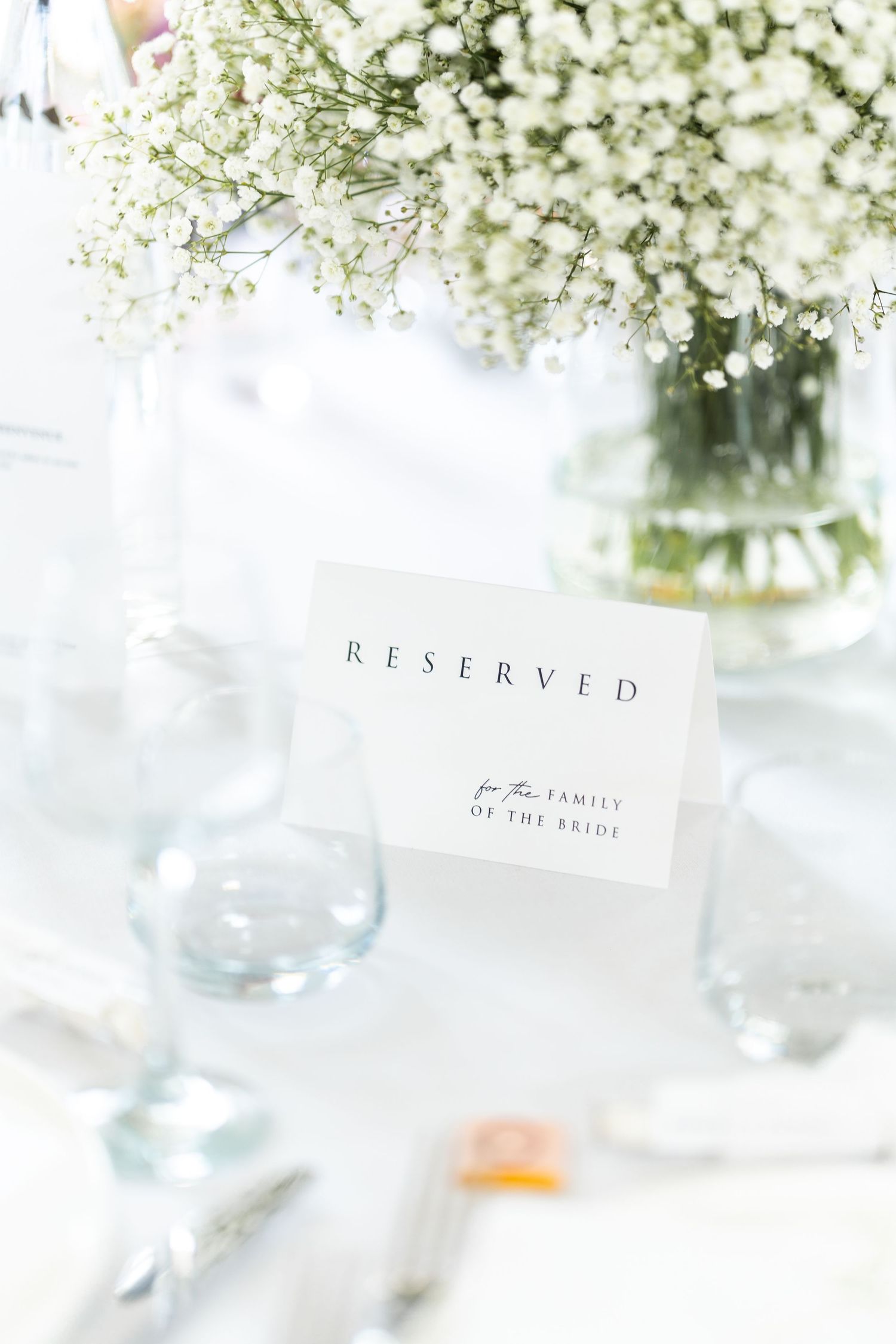 Elegant reserved table sign with baby's breath flowers in a glass vase on a white tablecloth at a wedding reception.
