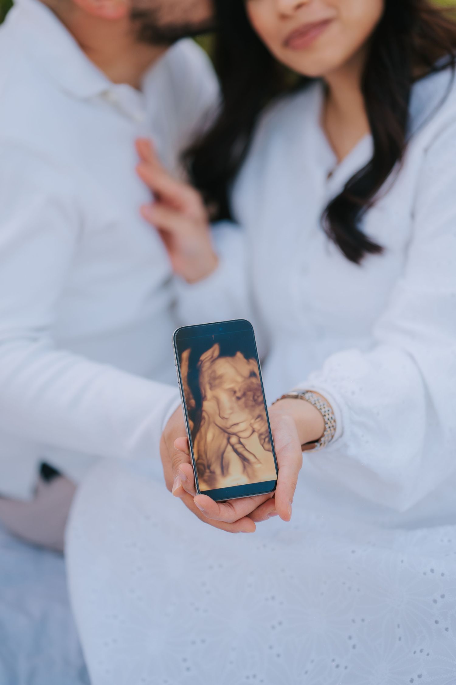 A smartphone displaying an ultrasound scan being held up in white-sleeved arms.
