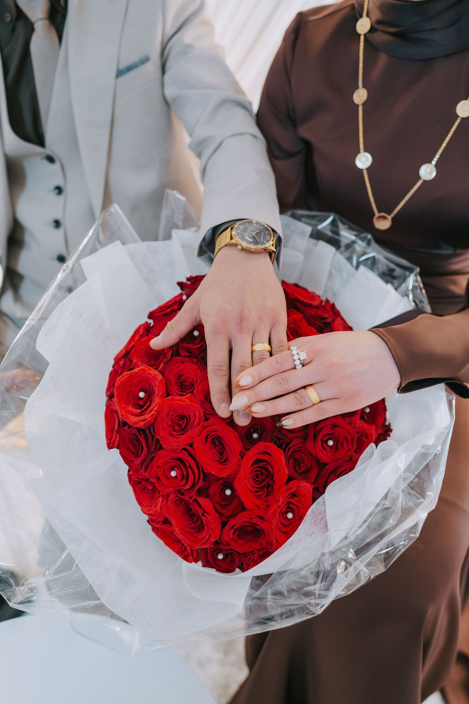 Hands displaying engagement ring over a beautiful bouquet of red roses wrapped in white paper.