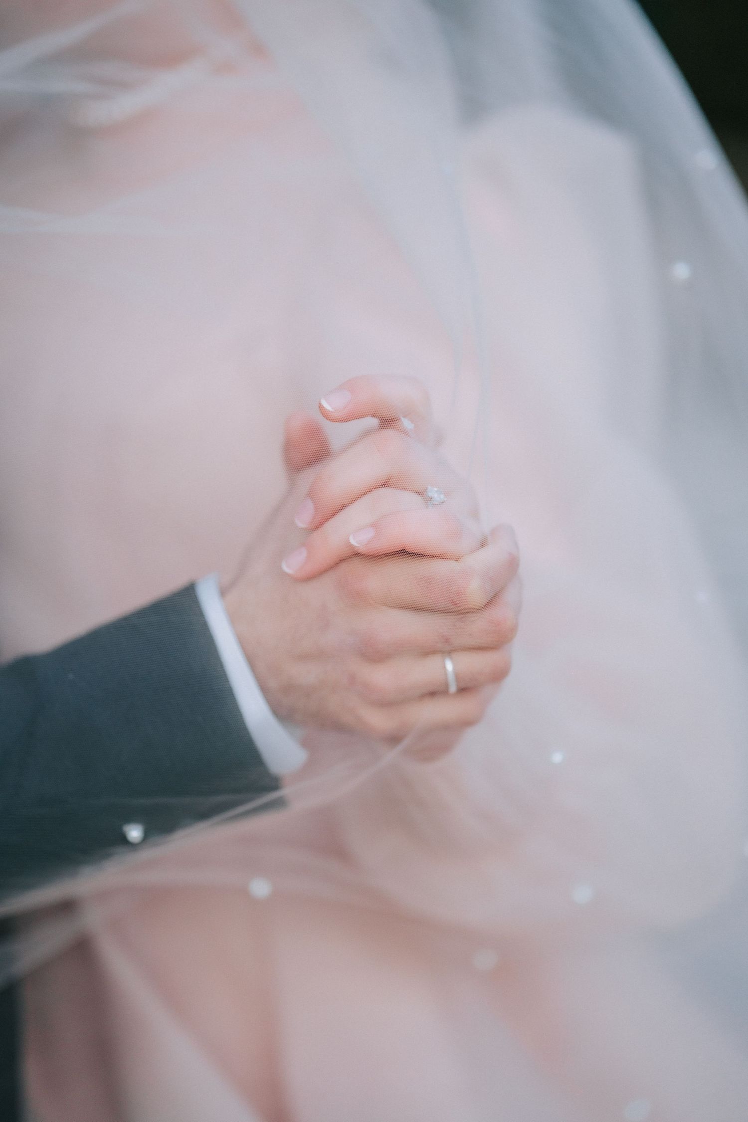 Close-up of clasped hands with wedding ring through delicate veil.