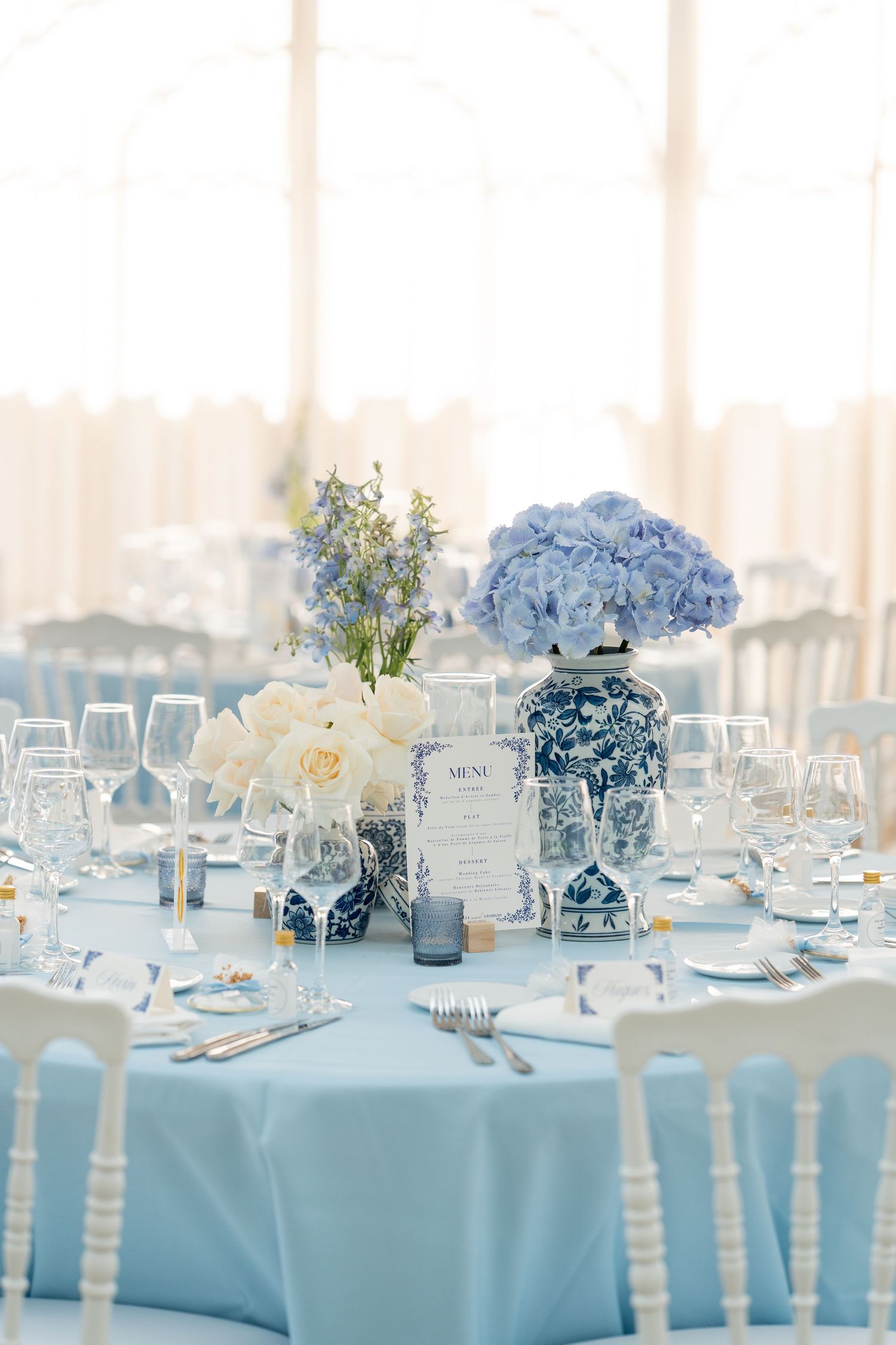 Elegant wedding reception tables decorated in light blue and white with floral centerpieces and crystal glassware.