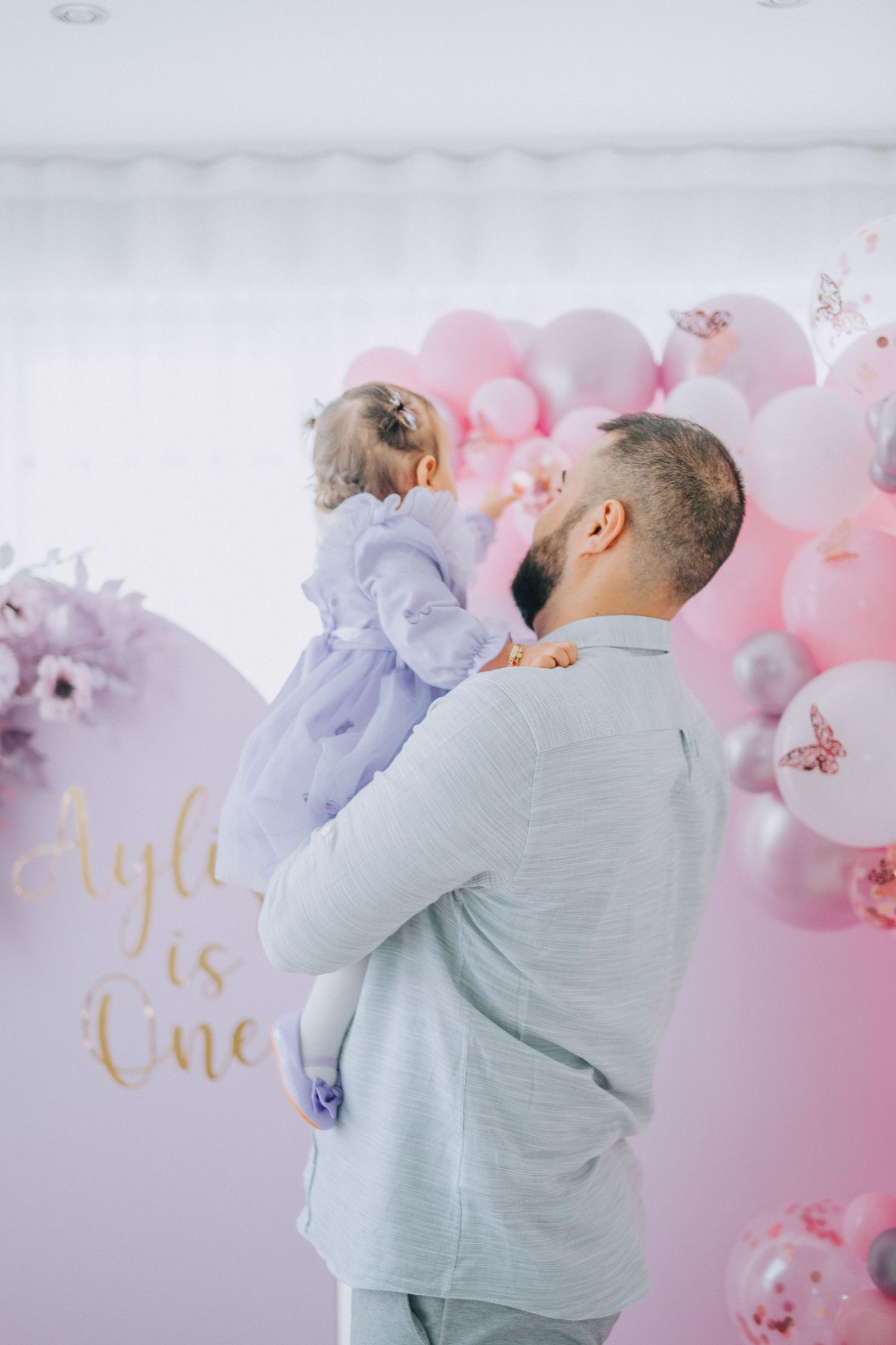 First birthday celebration with pink and white balloon arch backdrop and floral decorations.