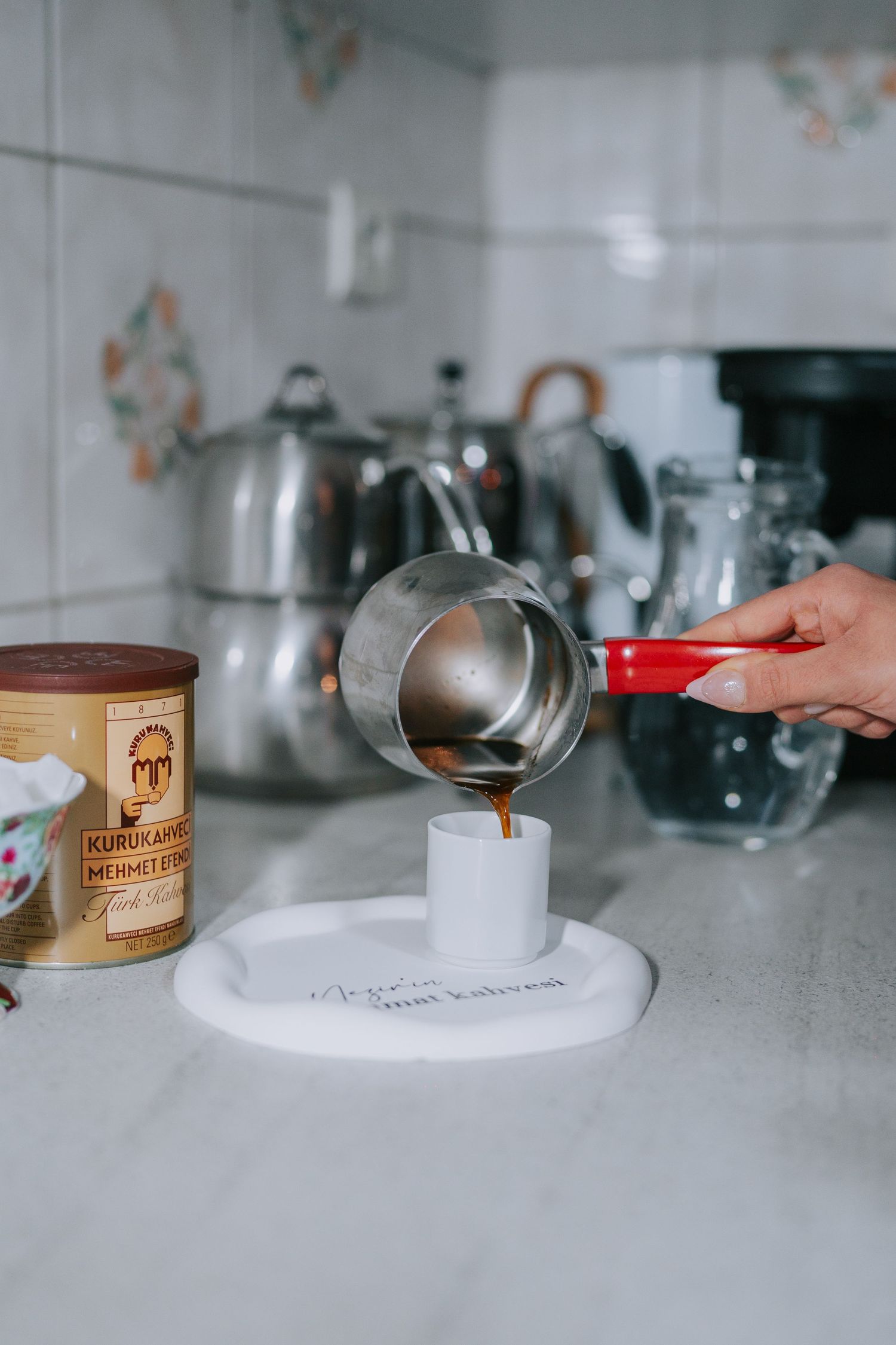 Coffee being poured into a small white cup on a kitchen counter.