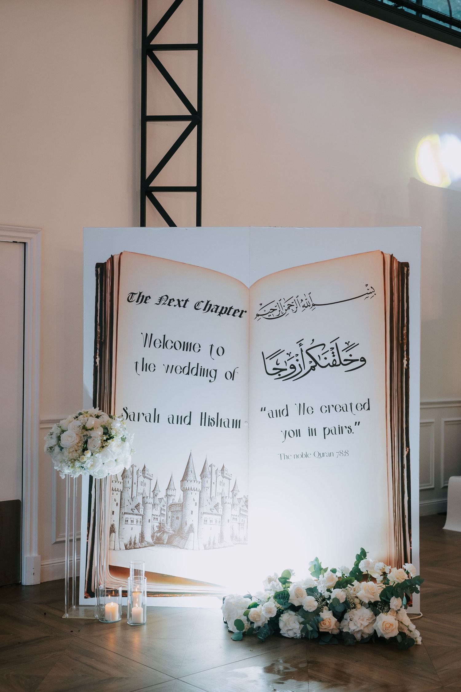 A large decorative wedding welcome sign designed like an open book with Arabic calligraphy and floral arrangements.