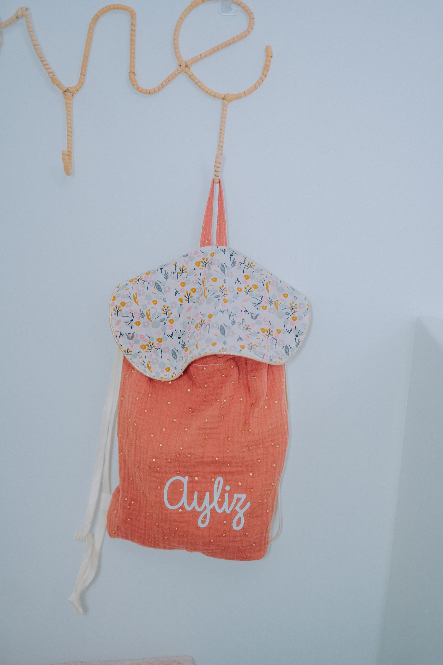 Peach colored decorative bag with floral pattern hanging against white wall.