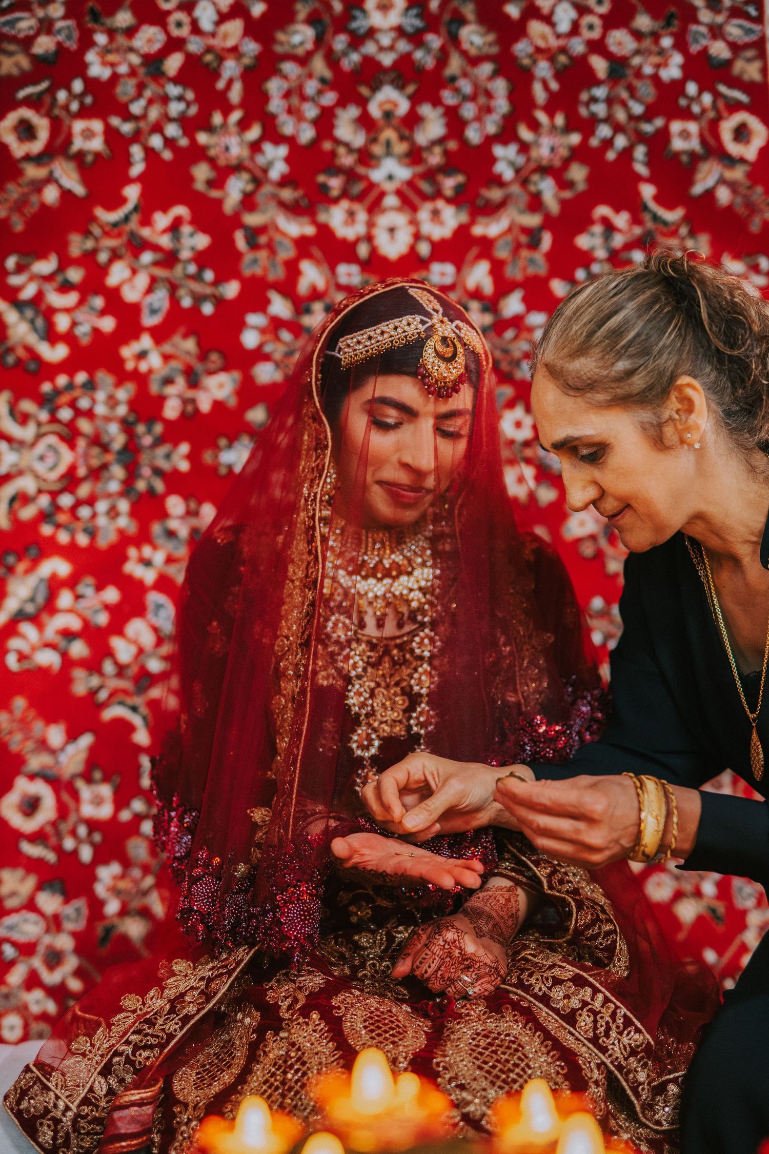 Wedding preparation scene with traditional bridal attire against red patterned backdrop.