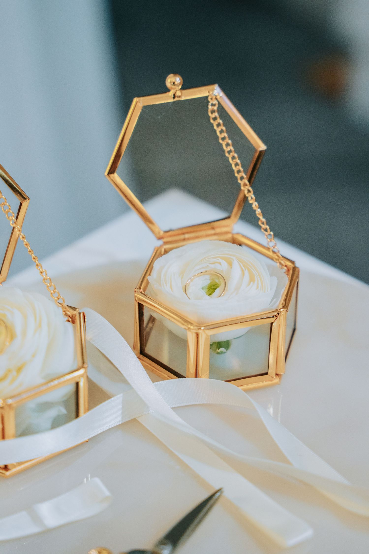 Gold hexagonal jewelry box with white rose against light background.