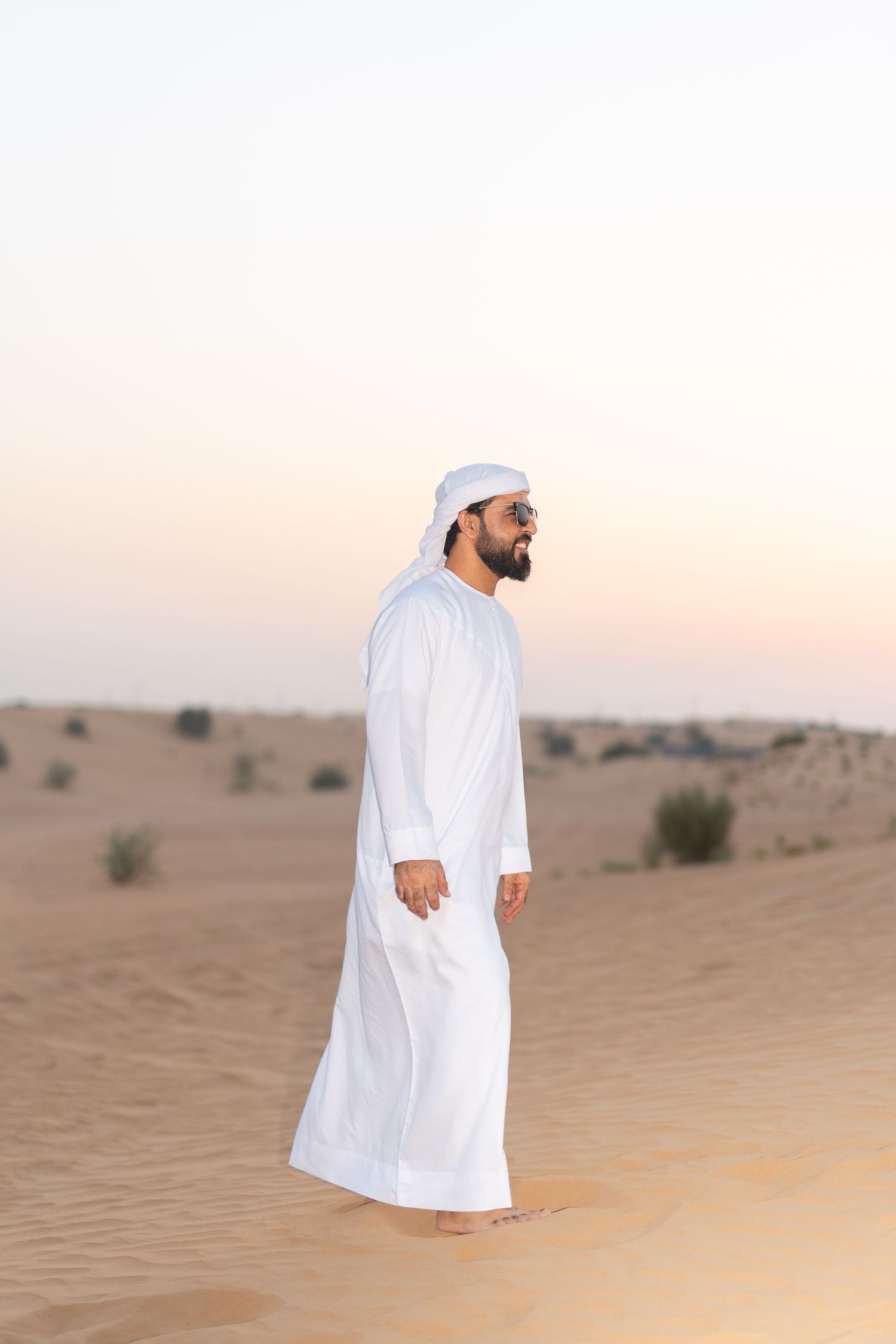Traditional dressed person standing on sand dunes during sunset in the desert.