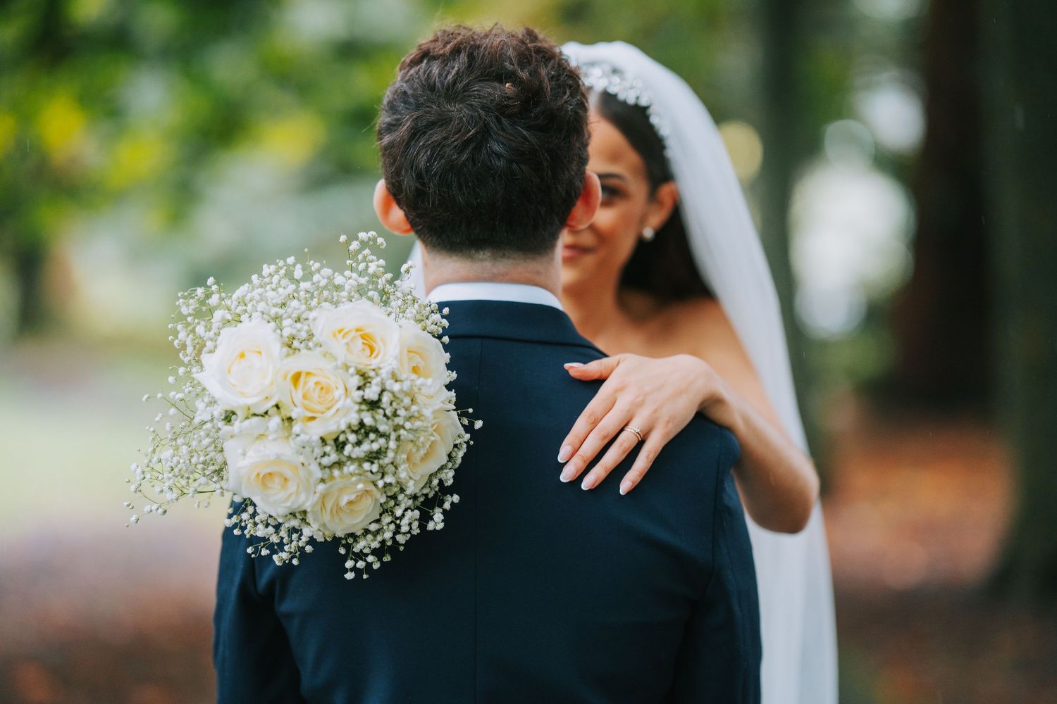 A tender candid wedding moment between newlyweds as they embrace outdoors with a delicate white floral bouquet.