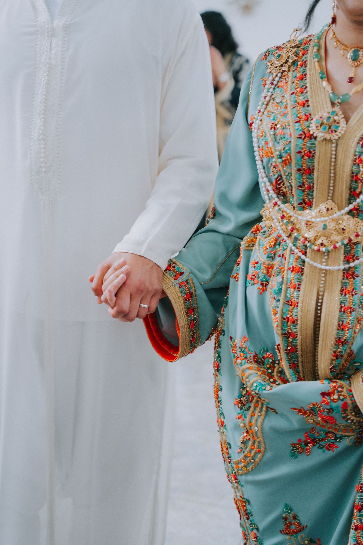 Couple holding hands wearing contrasting white and turquoise traditional Moroccan wedding outfits.