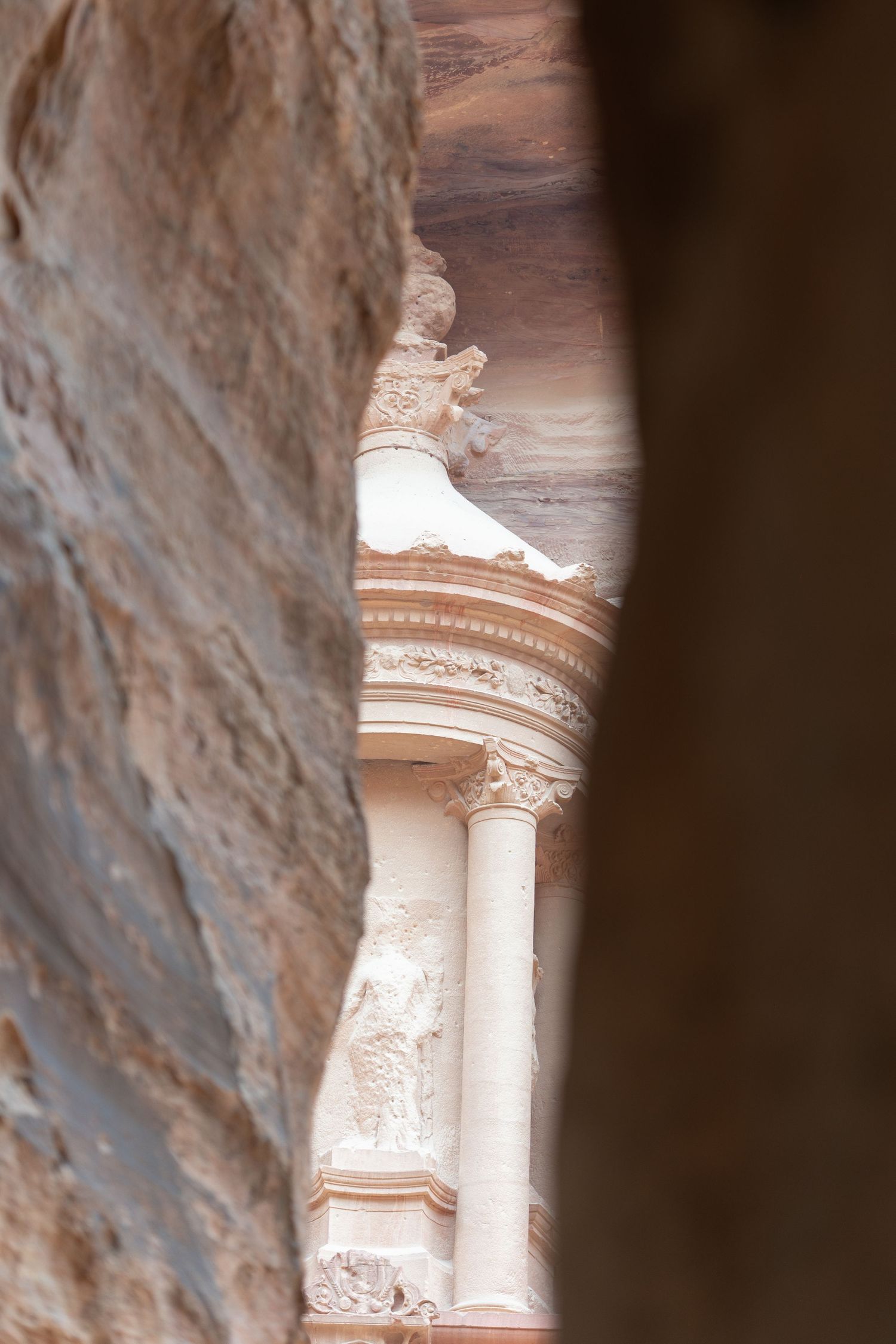 Ancient carved stone column and architectural details viewed through narrow passageway.