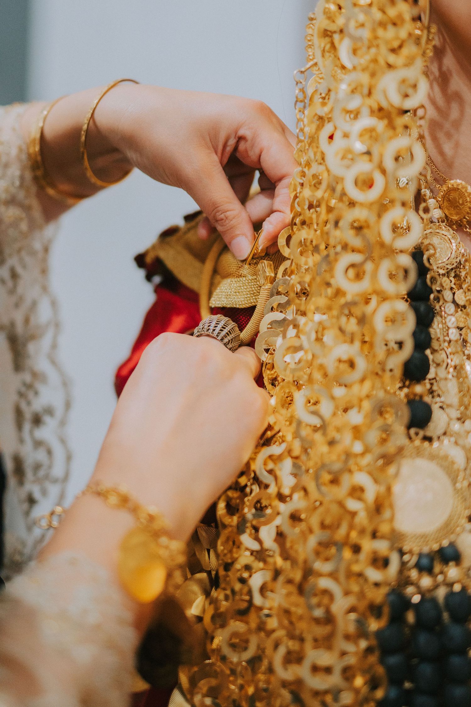 Hands adjusting elaborate golden jewelry and decorative elements of traditional attire.