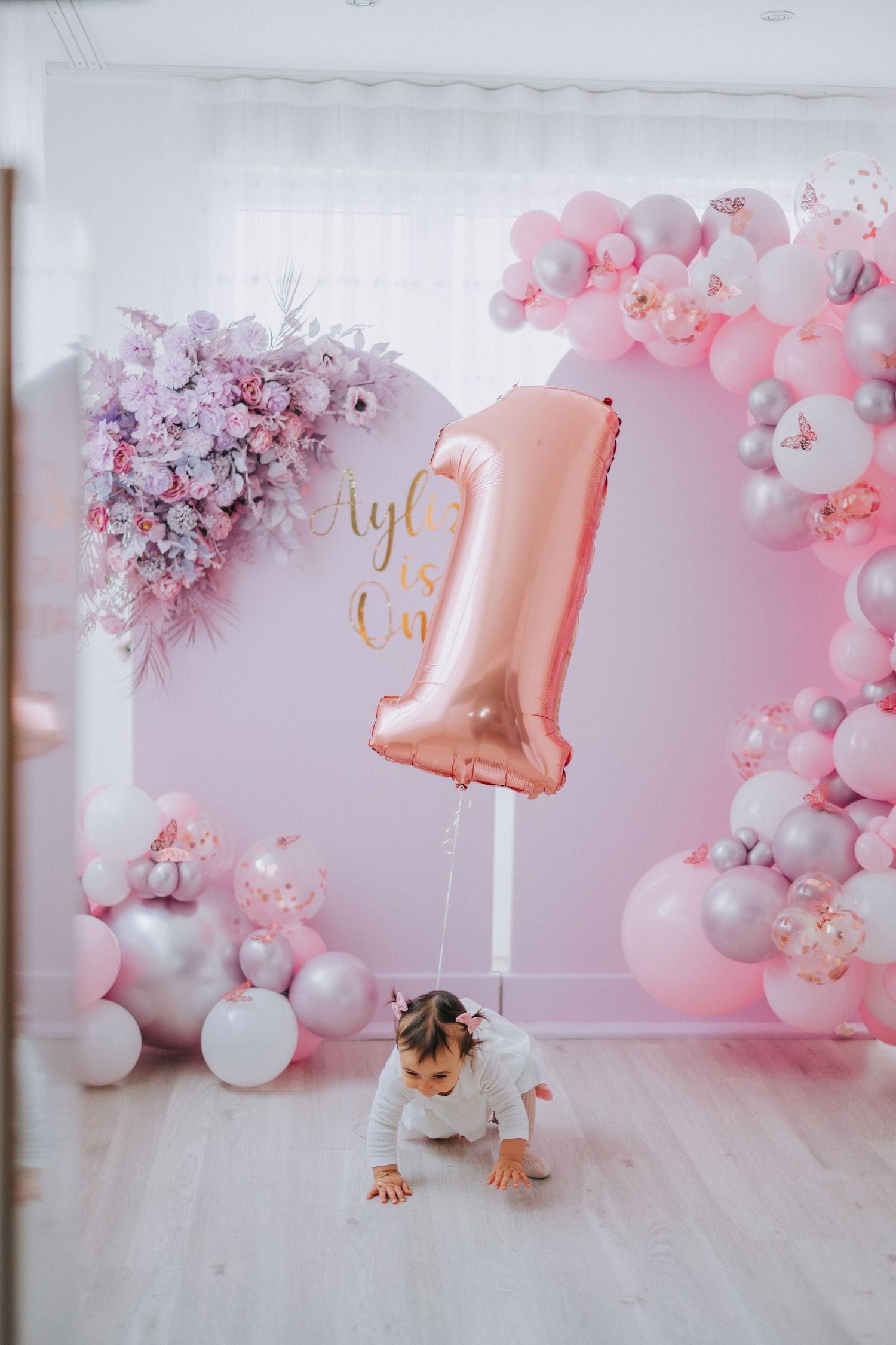 Rose gold number 1 balloon with crawling baby against pink balloon arch background.