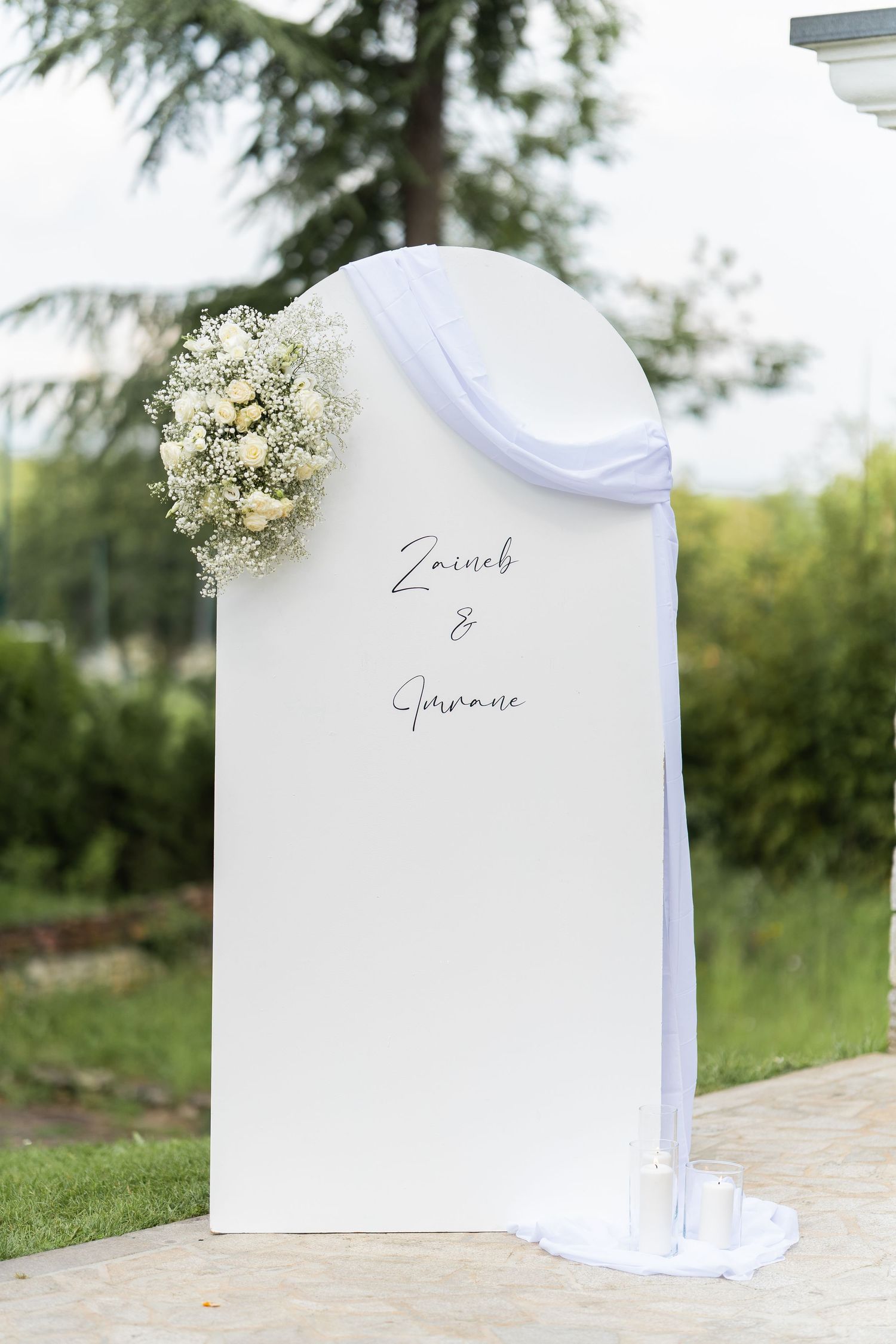 Elegant white wedding ceremony backdrop with draped fabric and baby's breath floral accent.