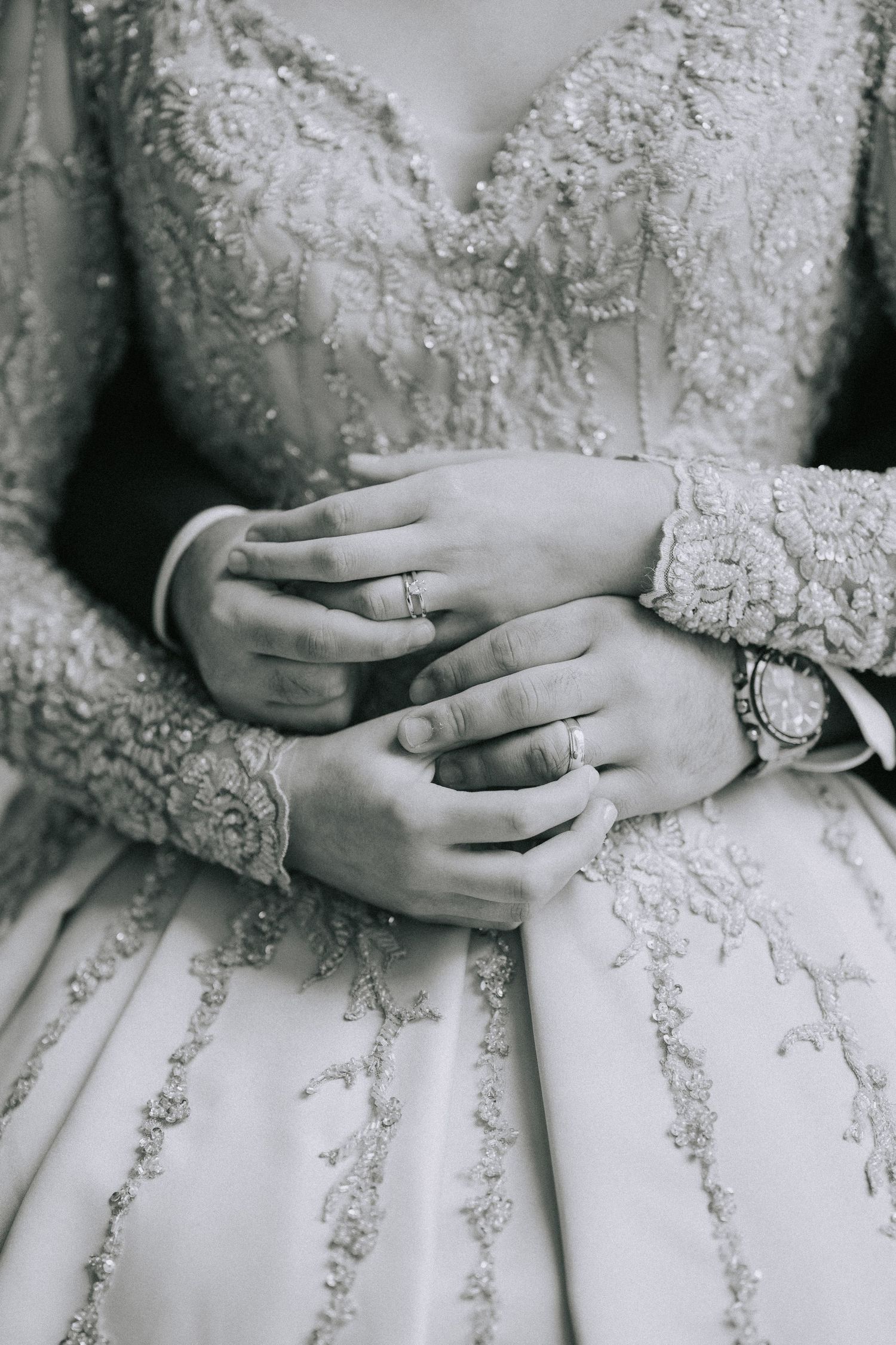 Close-up of lace wedding dress details and rings on hands.