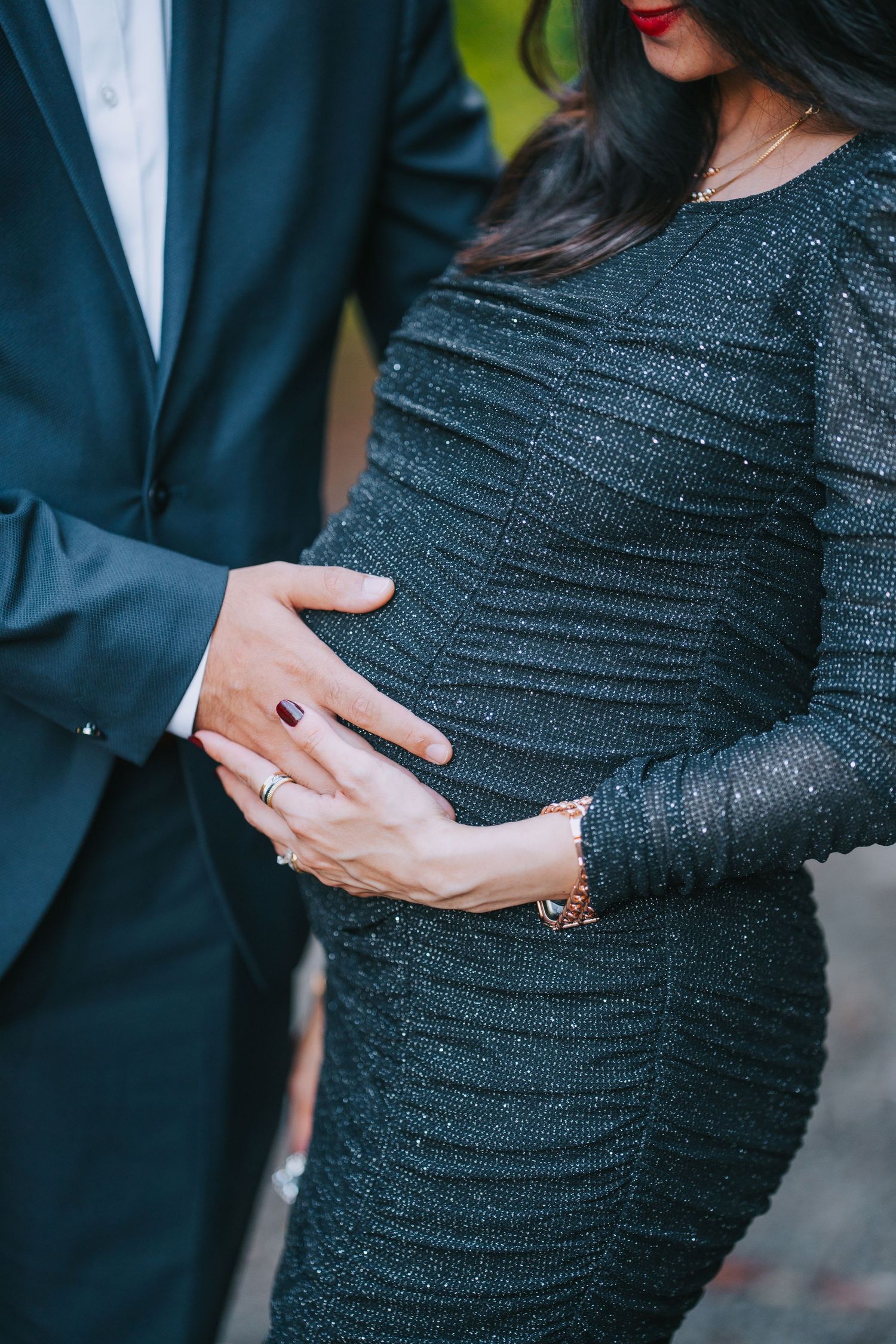 Close-up of hands resting on a textured black dress against a blurred natural background.