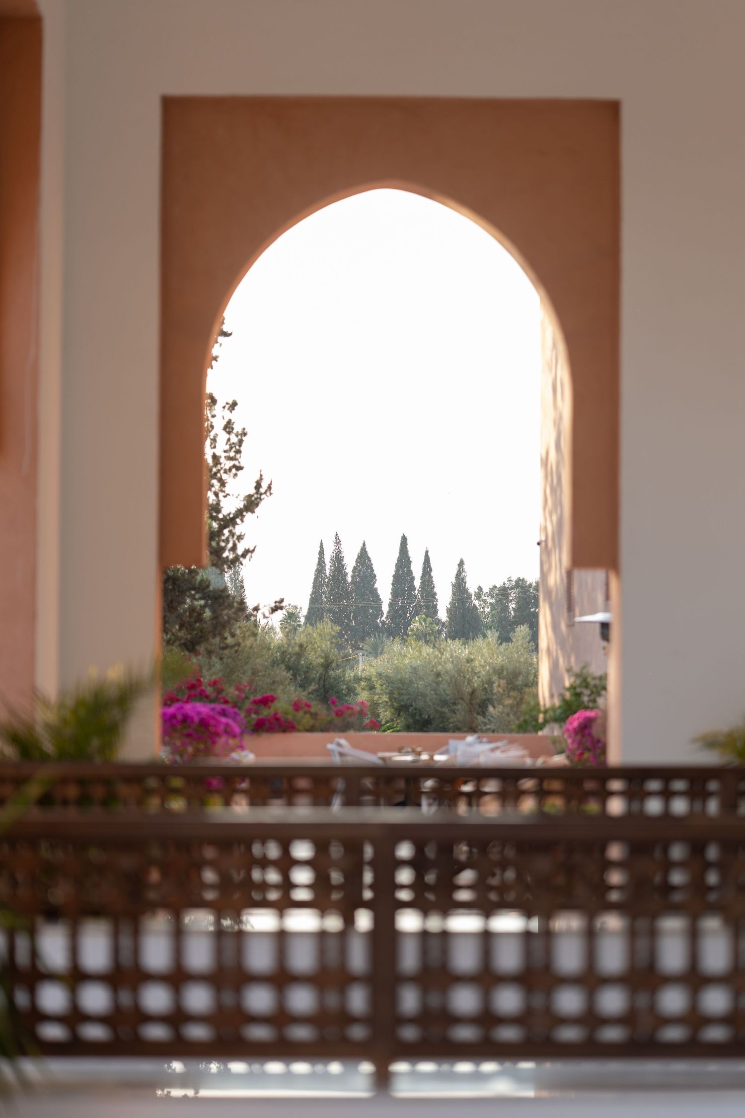 Arched doorway framing cypress trees and garden with pink flowers in Mediterranean setting.