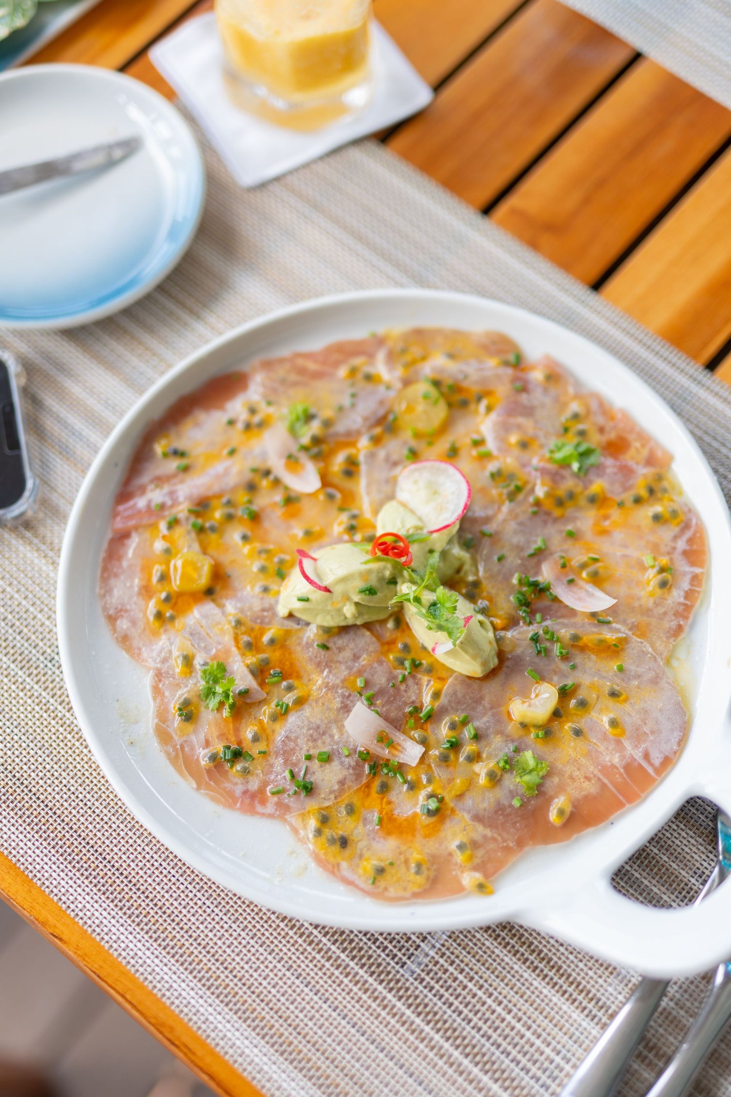 Elegant seafood carpaccio garnished with microgreens and citrus dressing served in a white dish.