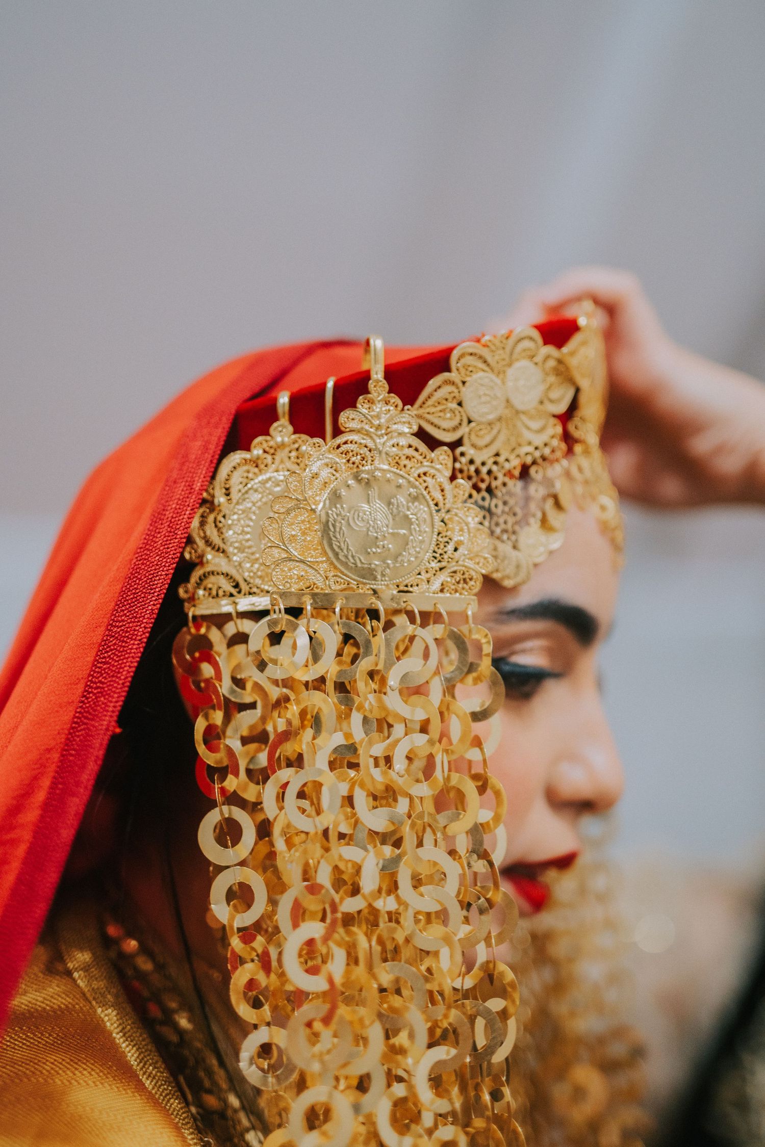 Detailed shot of ornate golden traditional headpiece with dangles against red fabric.