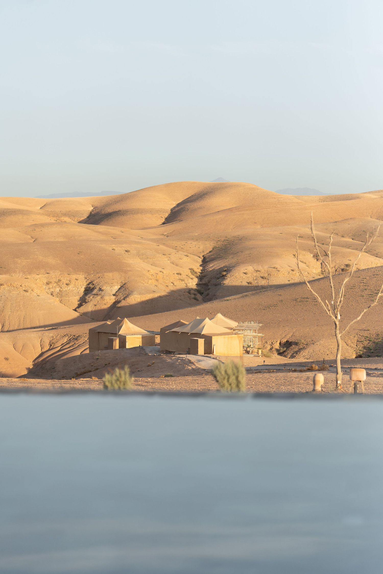 Desert oasis with buildings nestled among sandy dunes reflected in calm waters.
