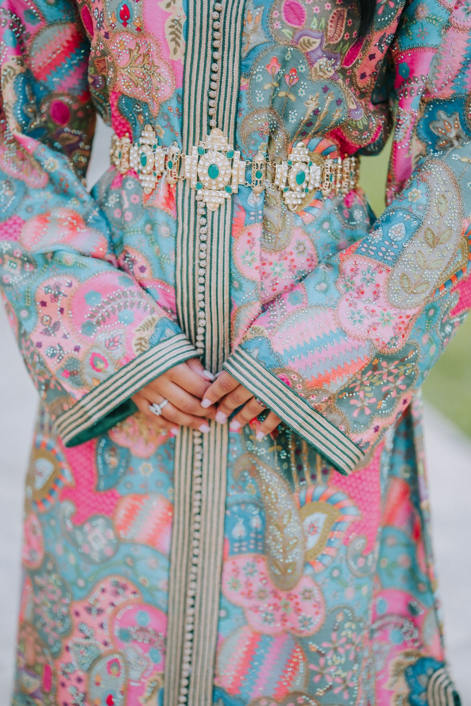 Close-up of a pink and turquoise kaftan with detailed embroidery and traditional belt decoration.