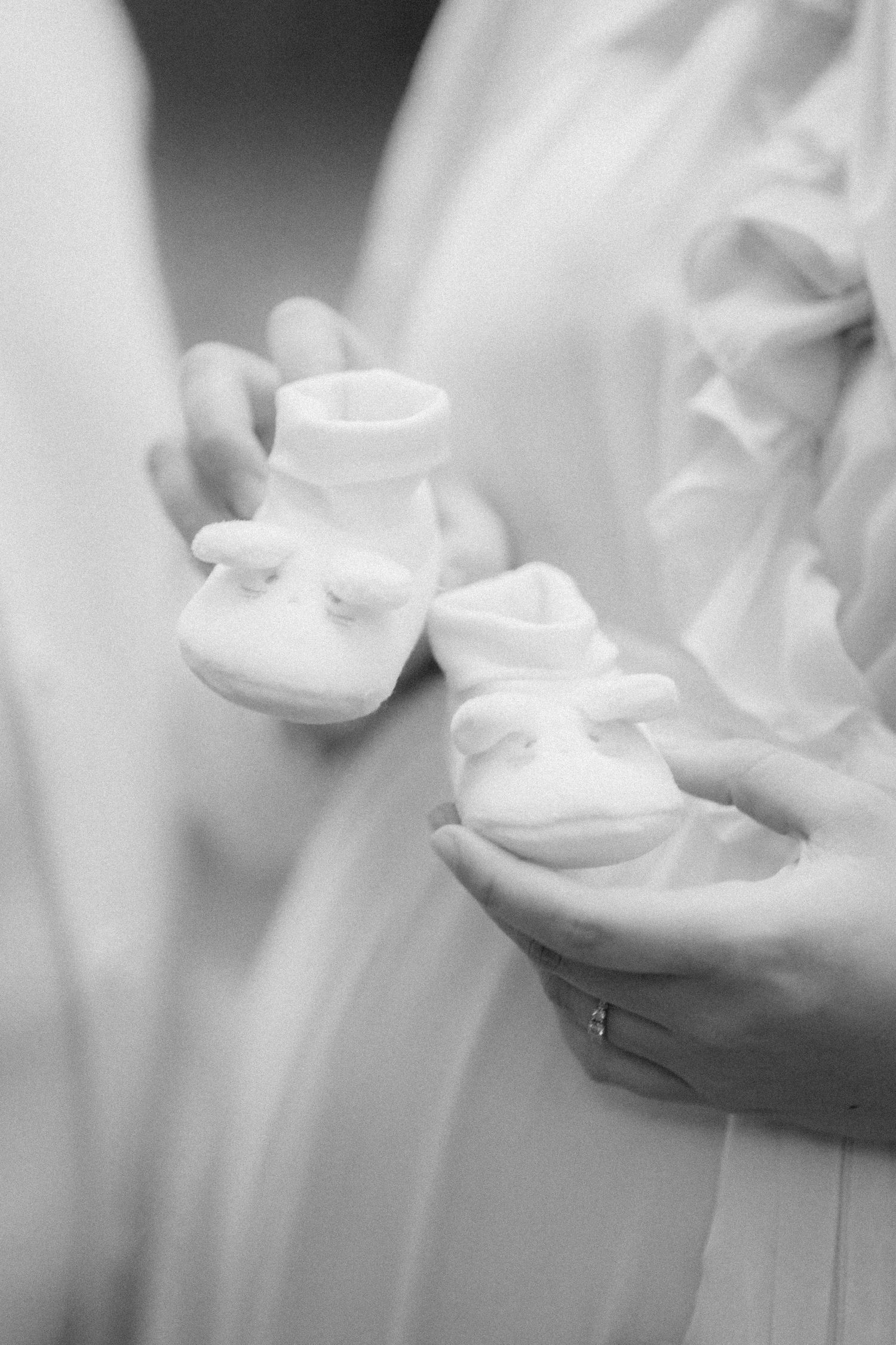 Gentle hands holding tiny white baby booties against flowing fabric.
