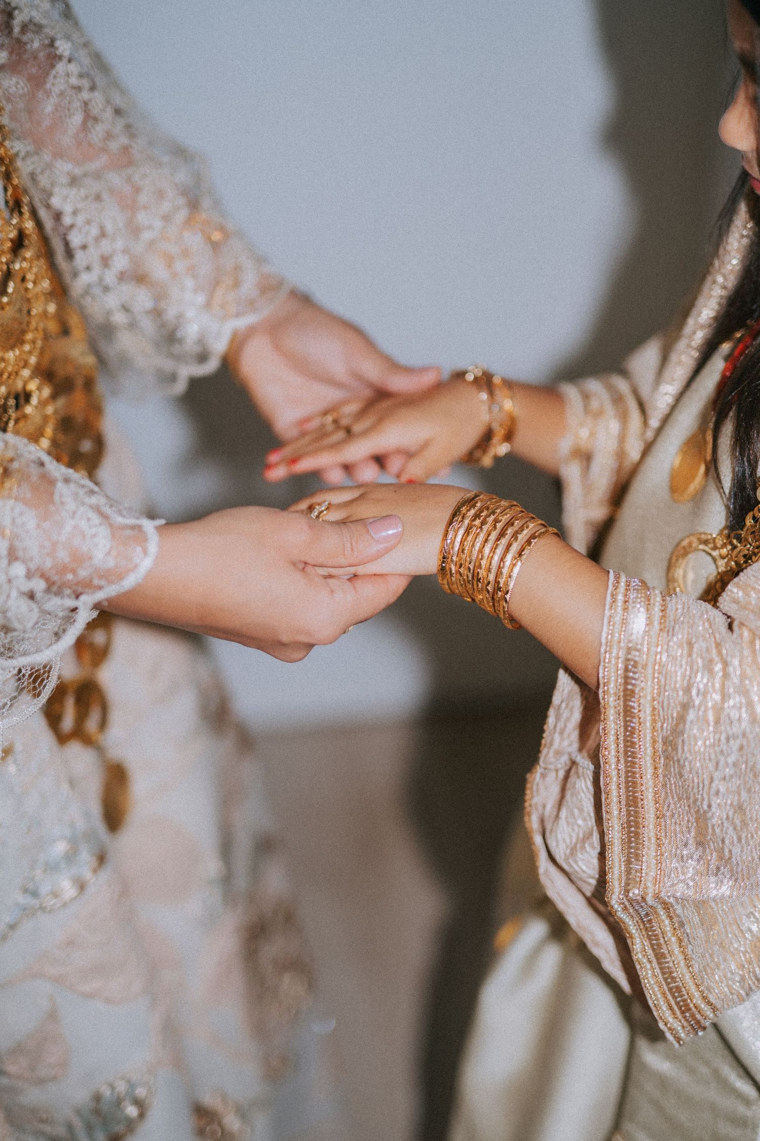 Two hands adorned with gold bangles and lace sleeves shown in intimate moment exchanging rings during traditional ceremony.