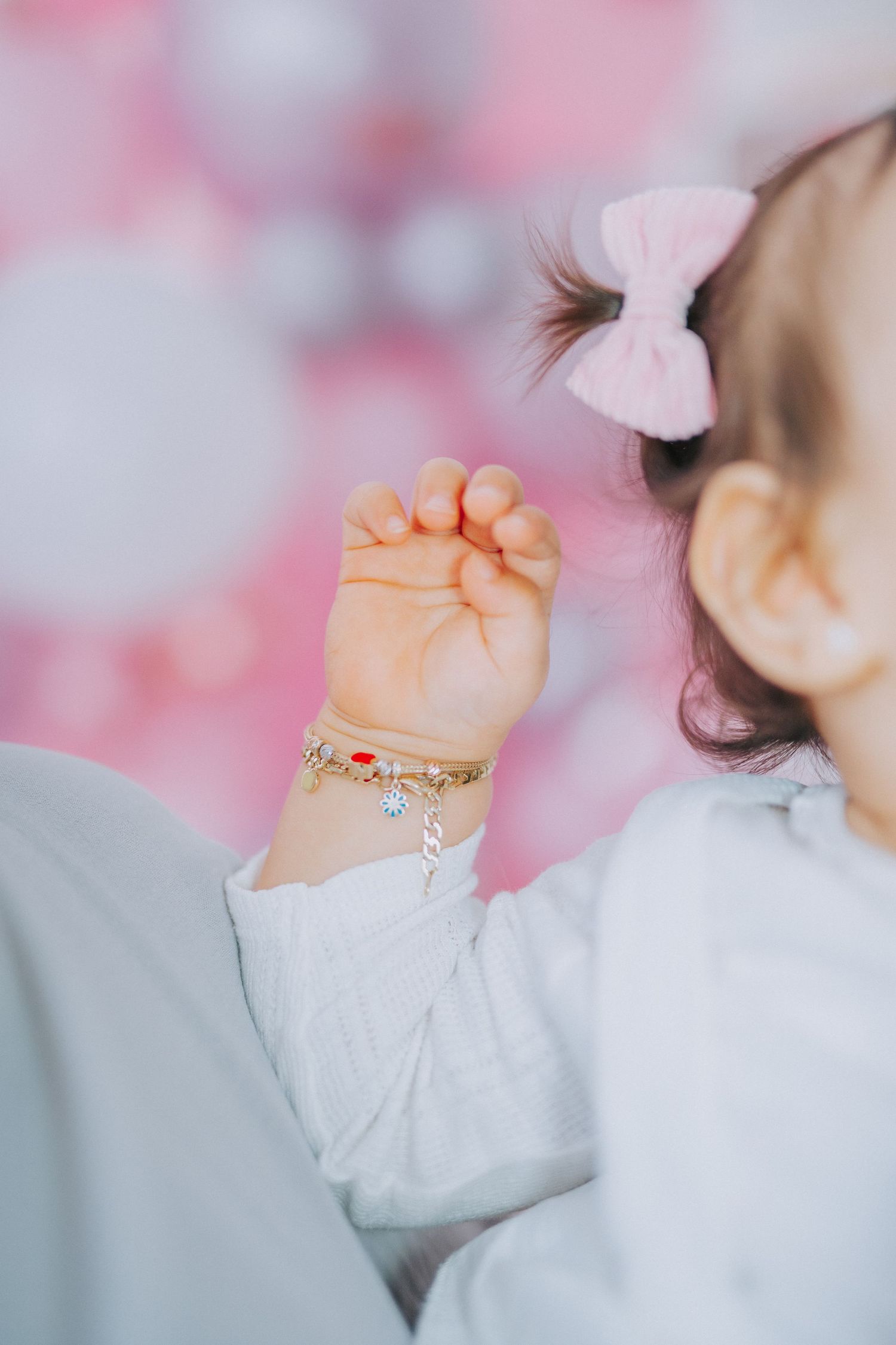 Baby's hand with delicate bracelet against pink blurred background.
