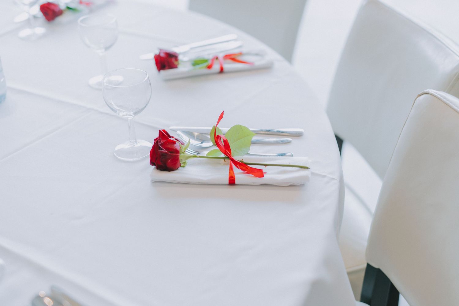 White table setting with red rose and ribbon decorated napkins.