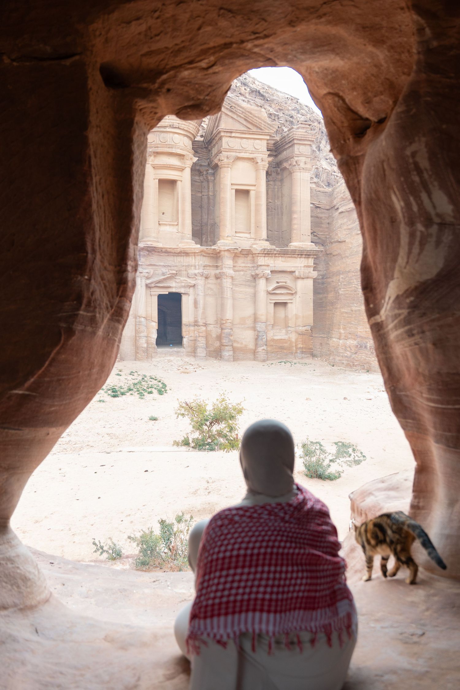 View through a cave opening of the ancient Monastery at Petra, Jordan, with someone watching from the shadows.