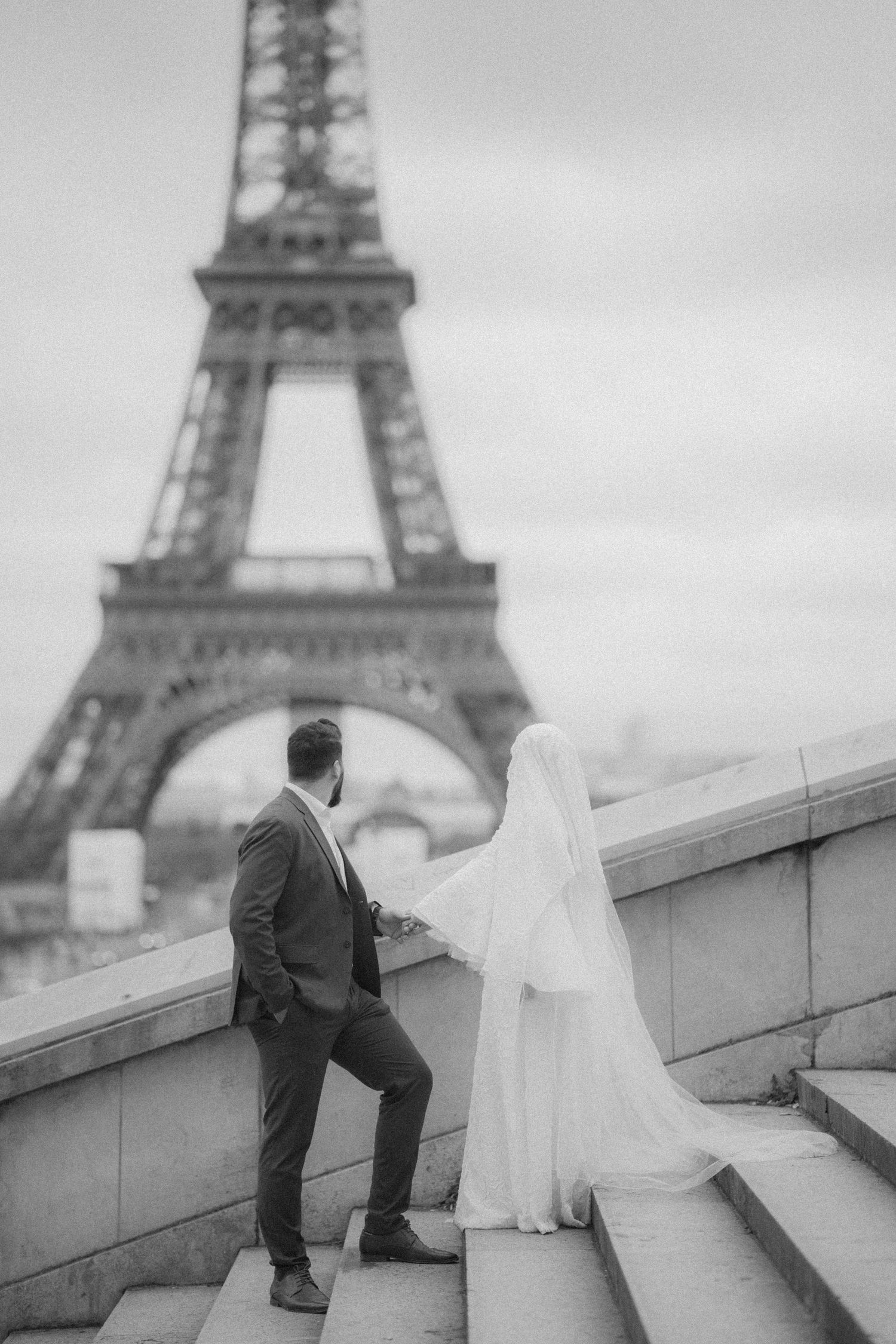 A black and white wedding photo featuring a couple posing on steps with the Eiffel Tower in the background.