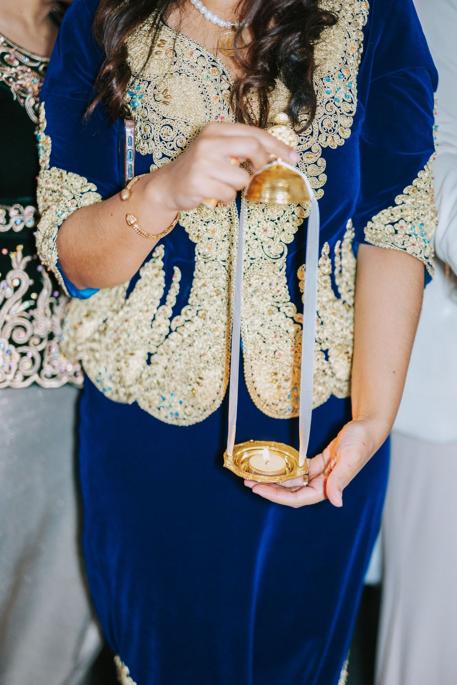 Detailed shot of ornate blue velvet dress with gold embroidery holding decorative item.