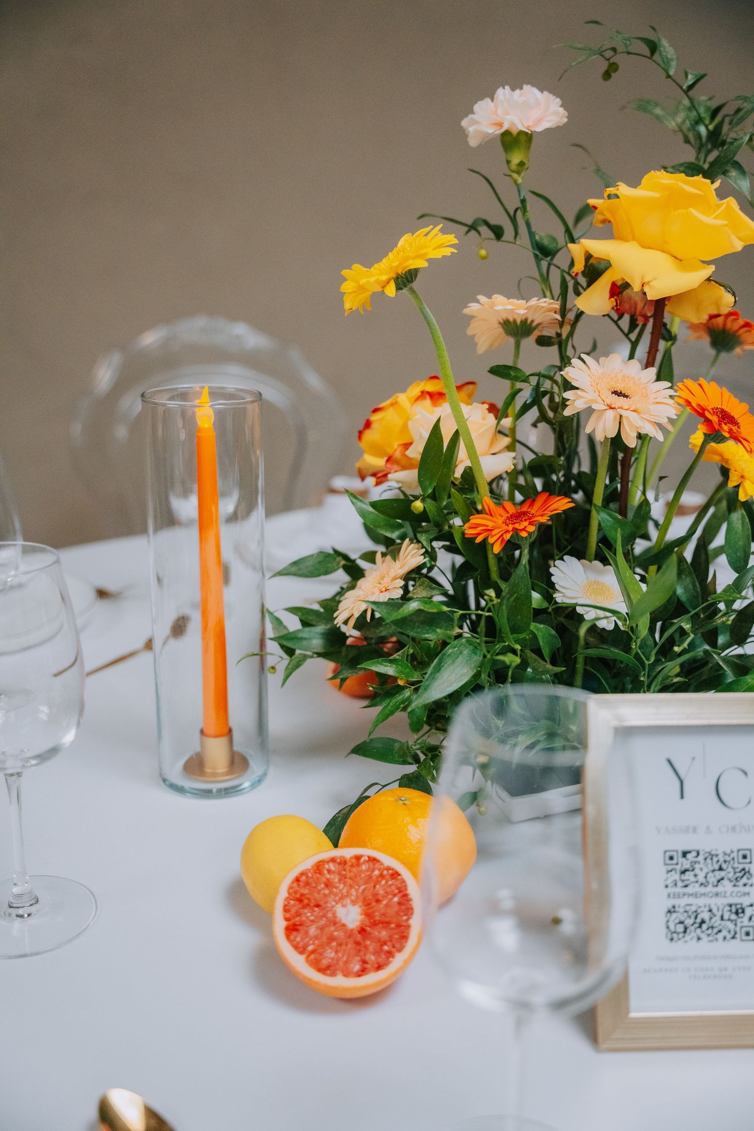Fresh floral centerpiece with yellow and orange blooms alongside grapefruit halves and a tall orange candle on white tablecloth.